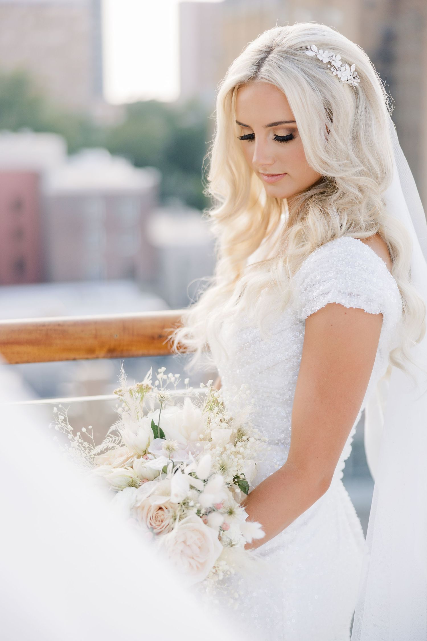 Side profile bridal portraits showcasing detailed lace gown and white floral bouquet in urban setting.