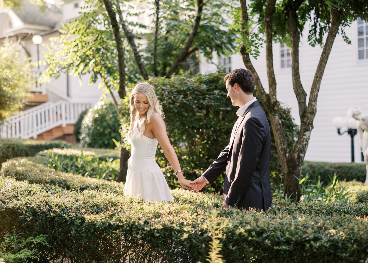 Sun-dappled garden path with elegant couple among trees and greenery.
