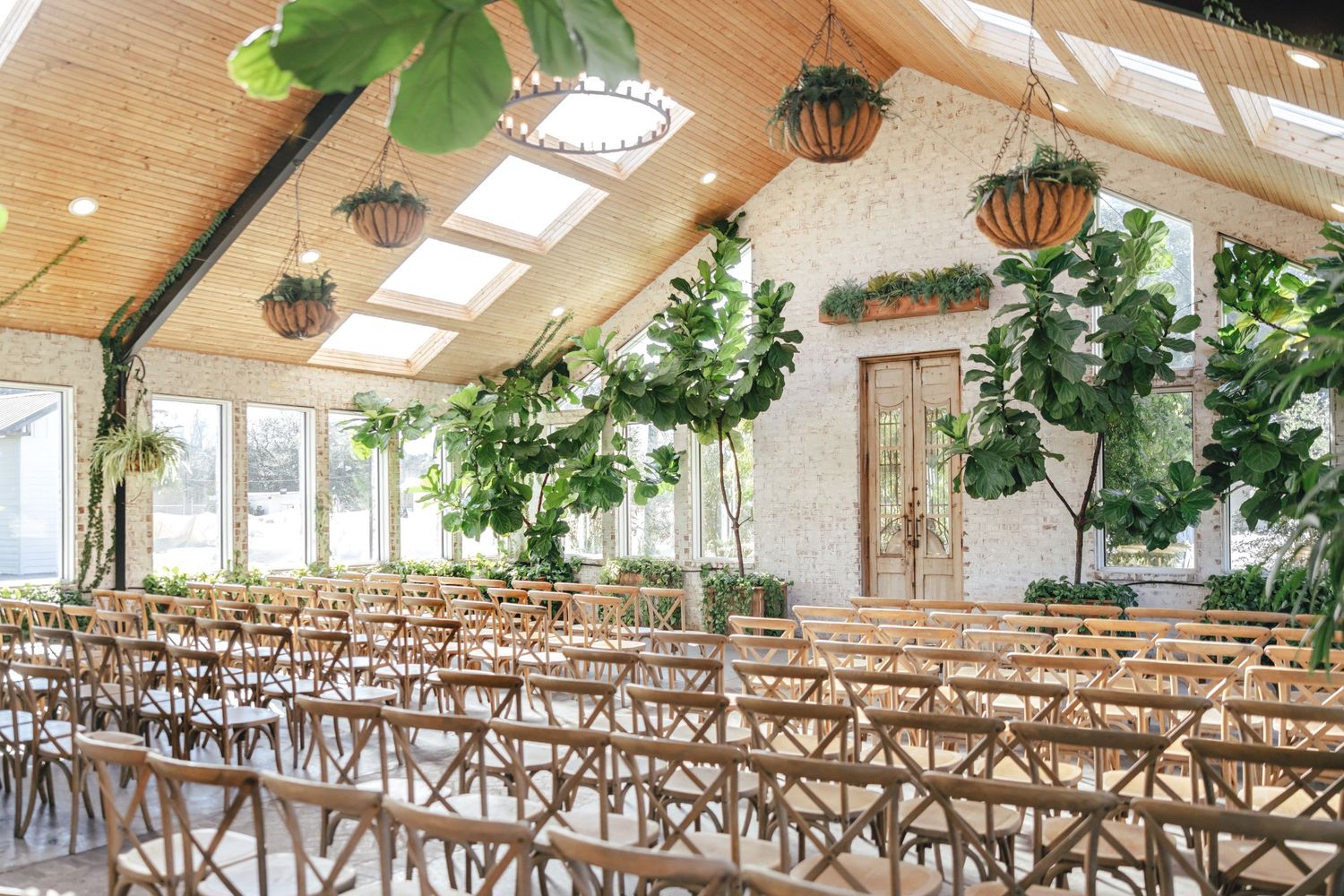 Rustic wedding venue interior with wooden cross-back chairs and hanging greenery decorations.