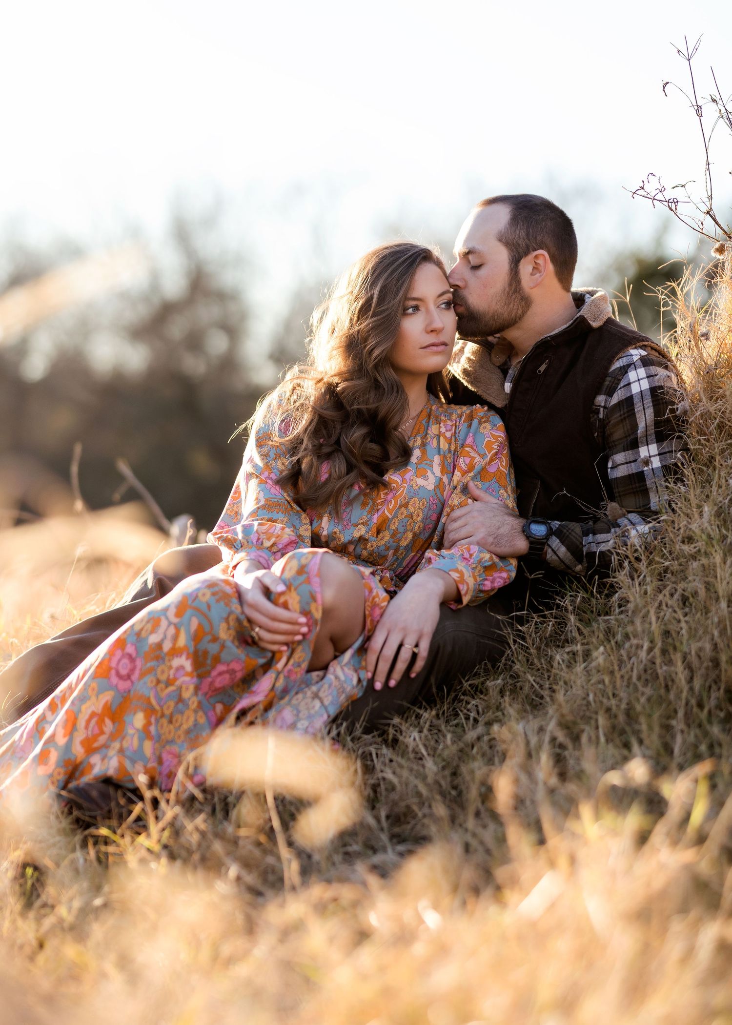 Romantic moment between couple sitting in tall grass at golden hour.