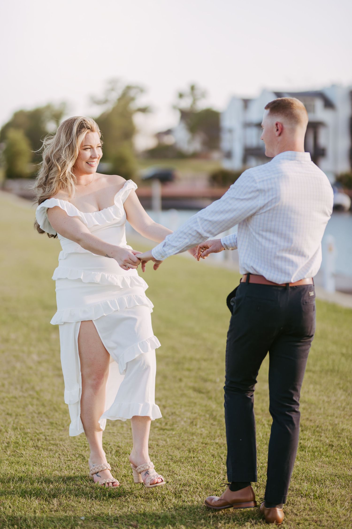 Couple dancing playfully on grass during sunset photo session.