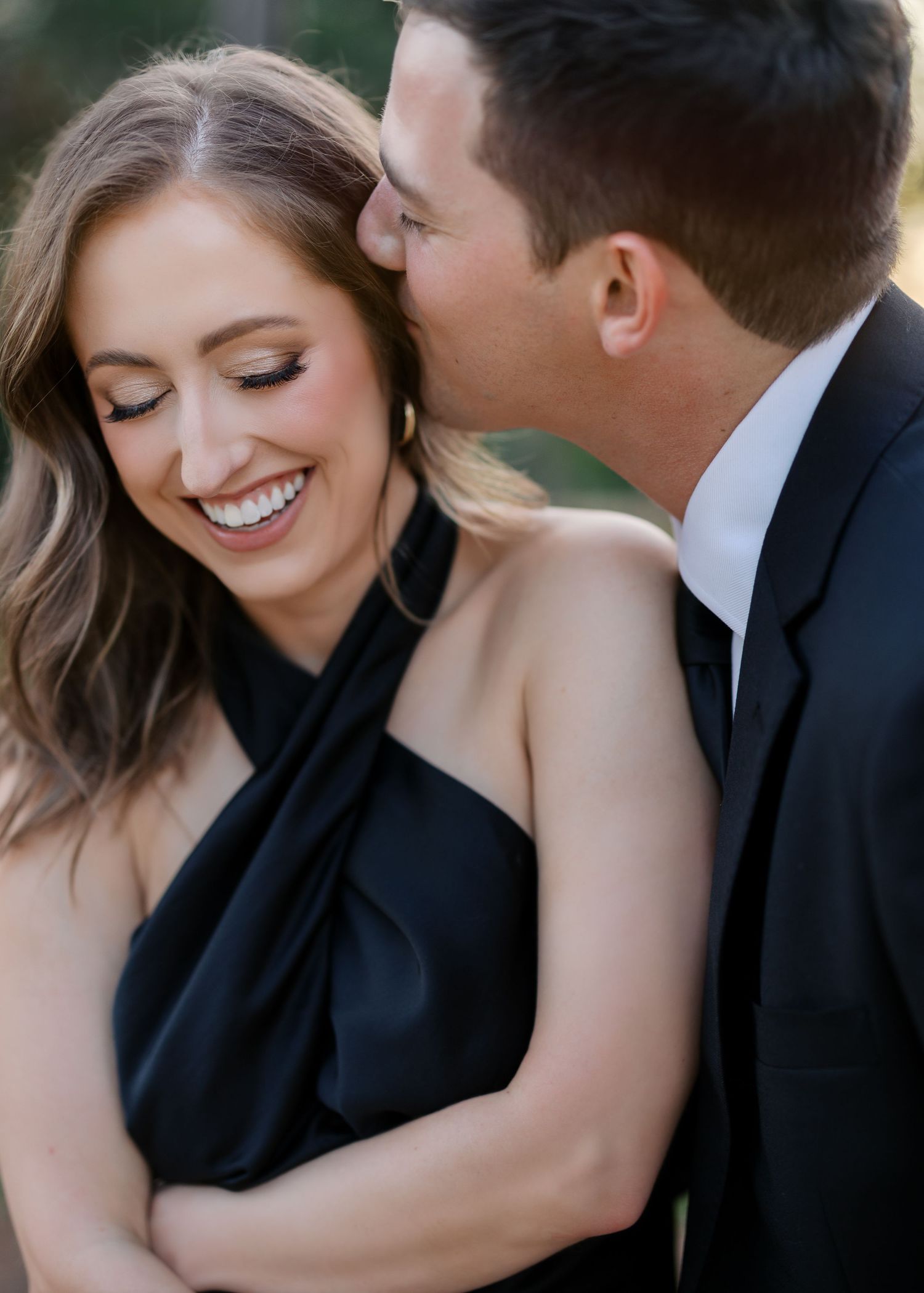 Romantic moment captured in elegant formal attire against a blurred natural background.
