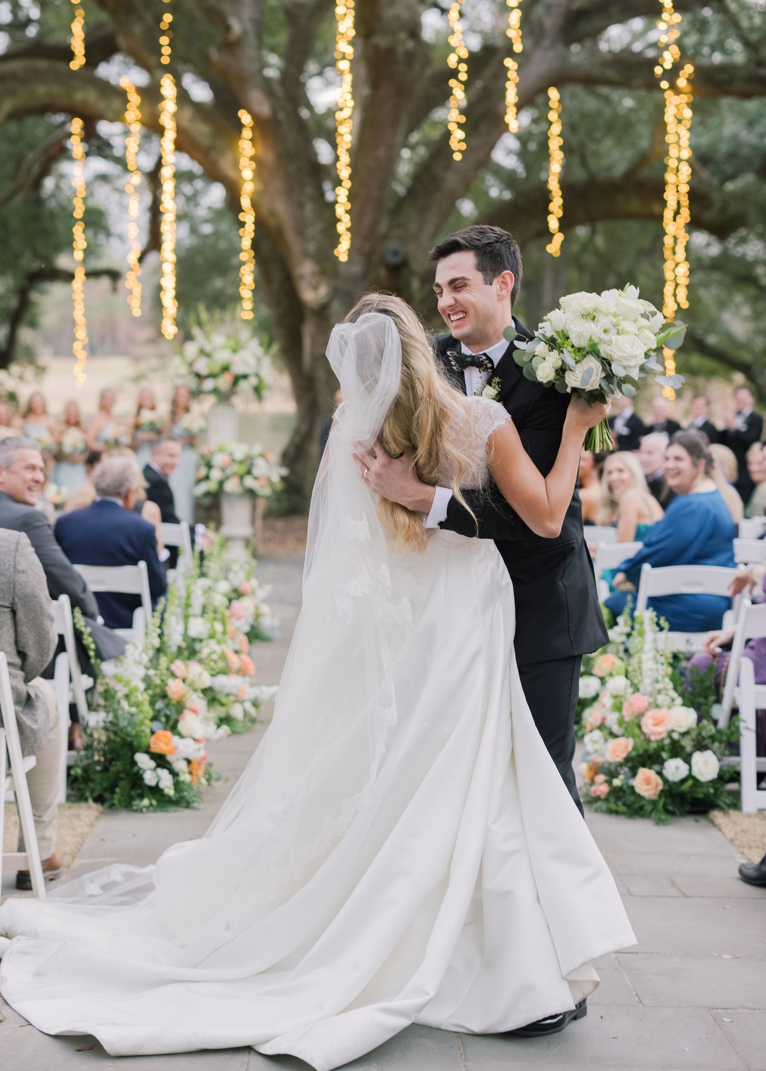 Wedding couple dances together on an outdoor patio decorated with hanging string lights and floral arrangements.
