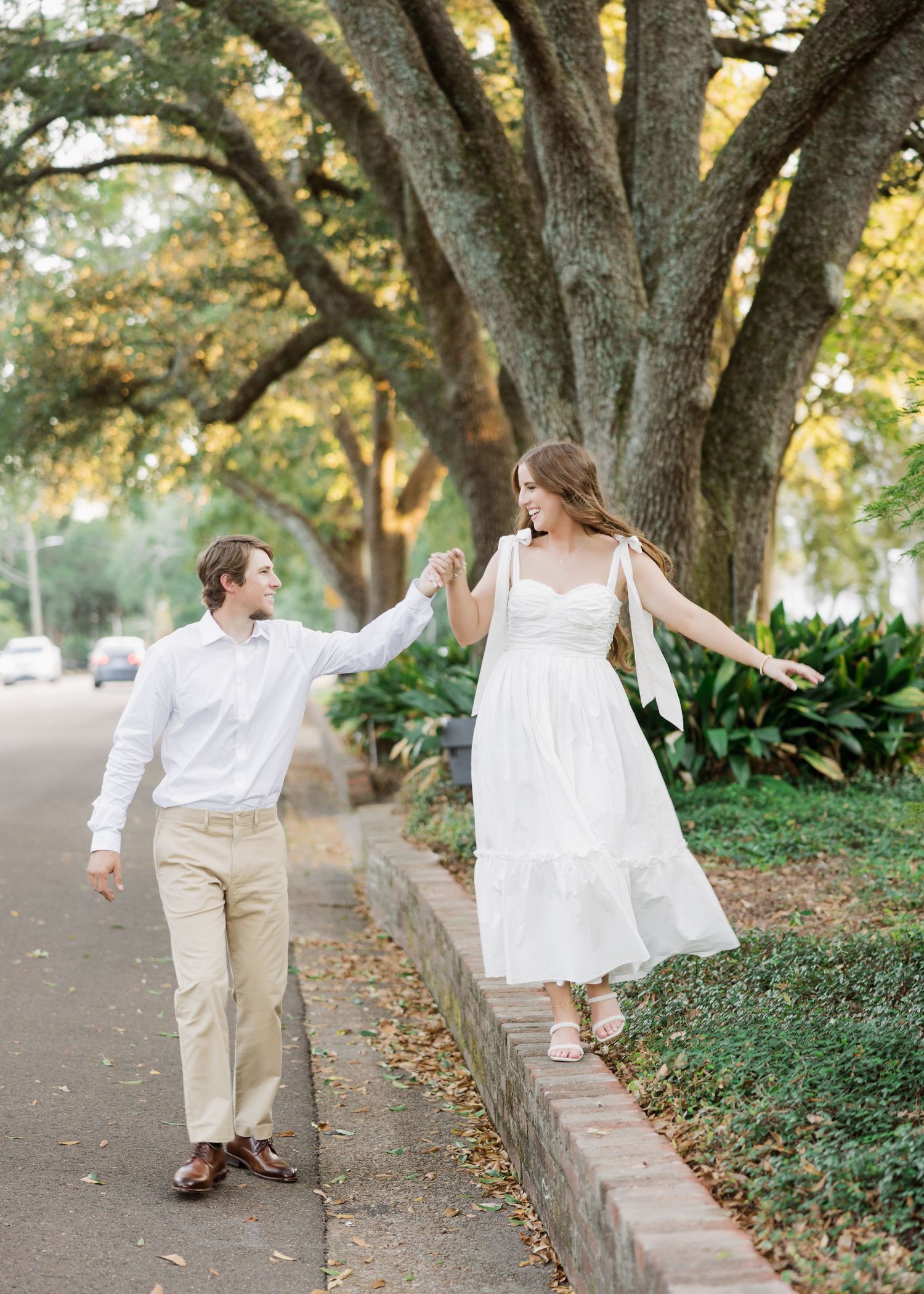 Joyful couple dancing together beneath large oak tree.