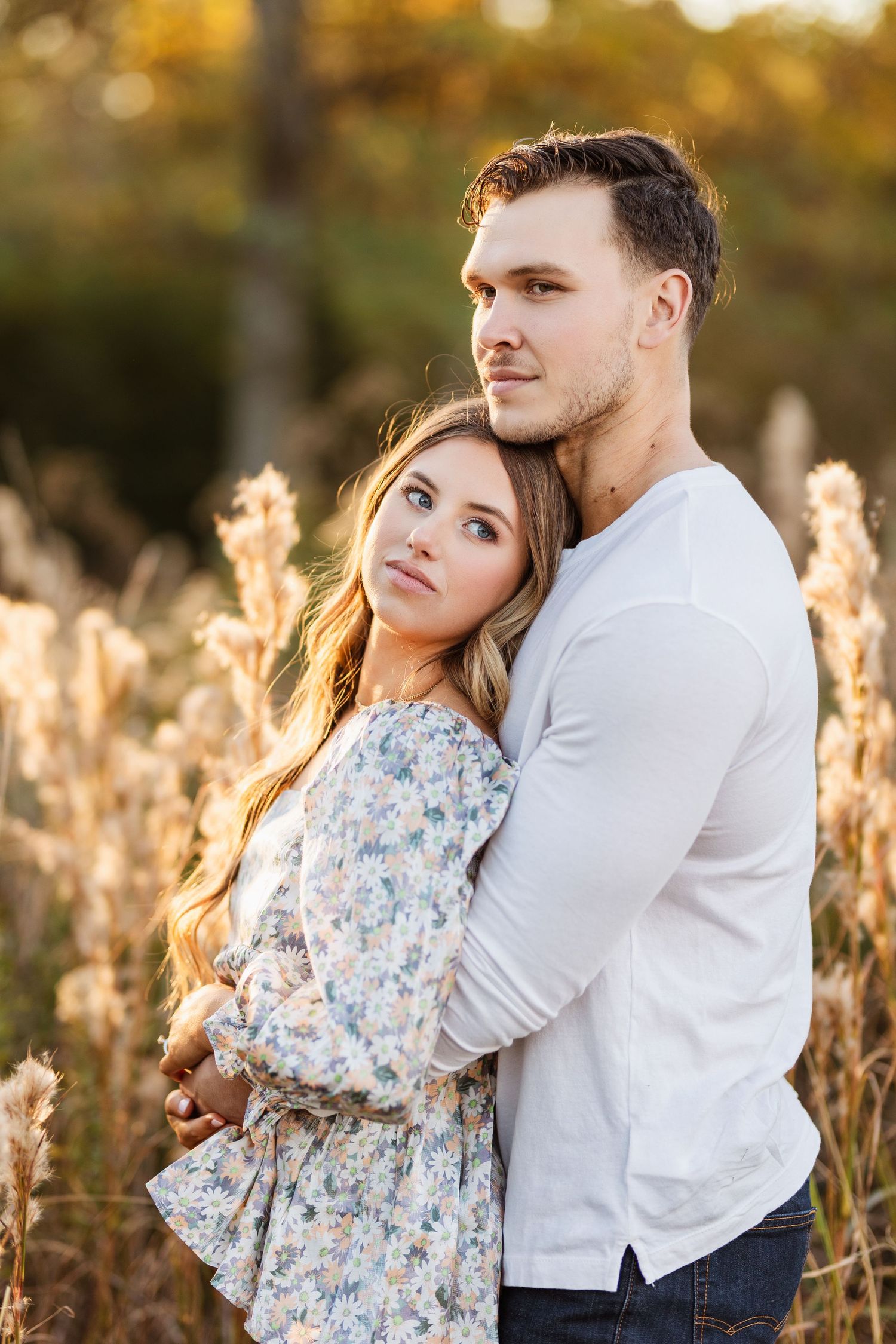 Romantic couple embracing in golden field during sunset photoshoot.