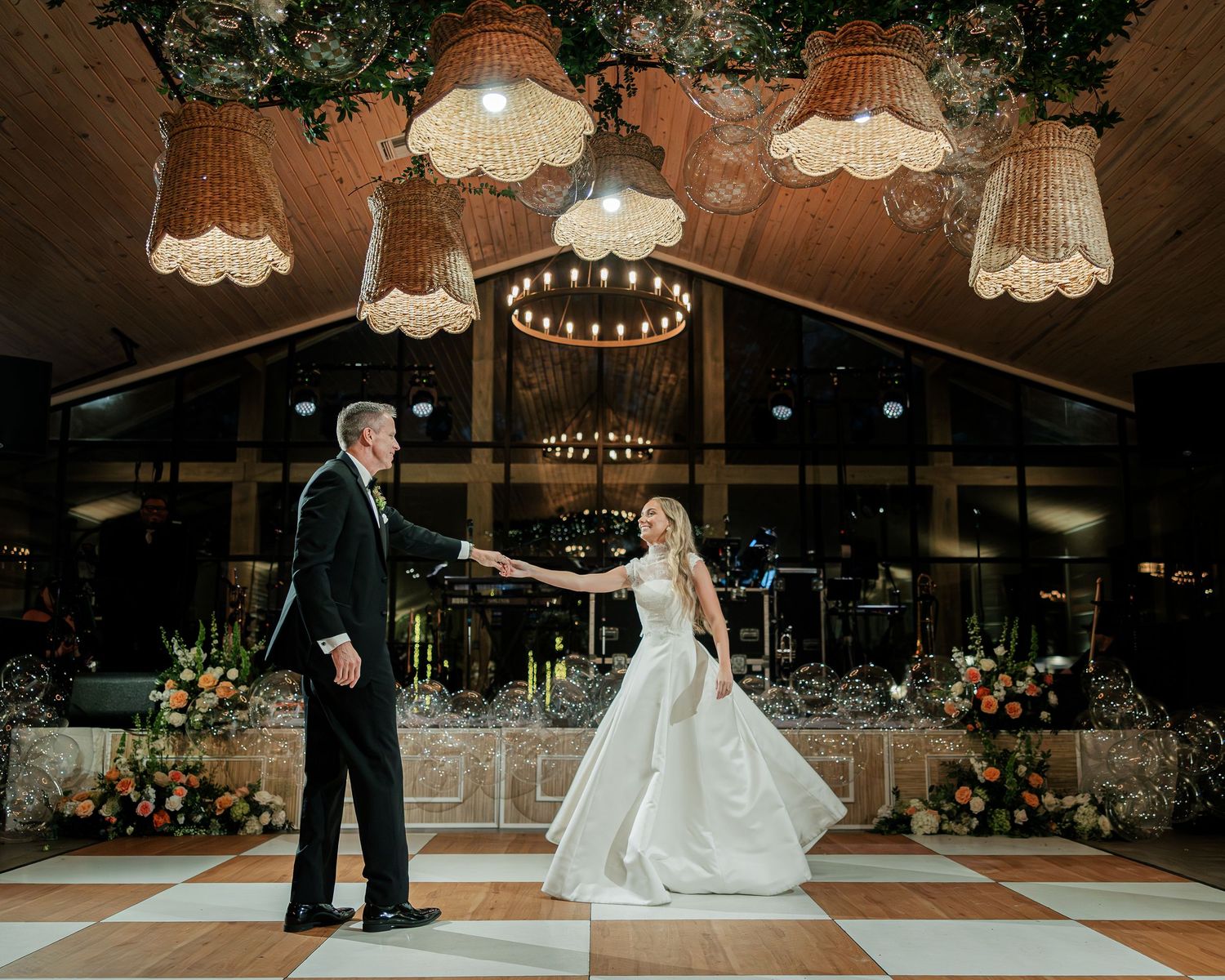 A couple shares their first dance on a wooden floor at an elegant wedding reception venue with hanging lights.