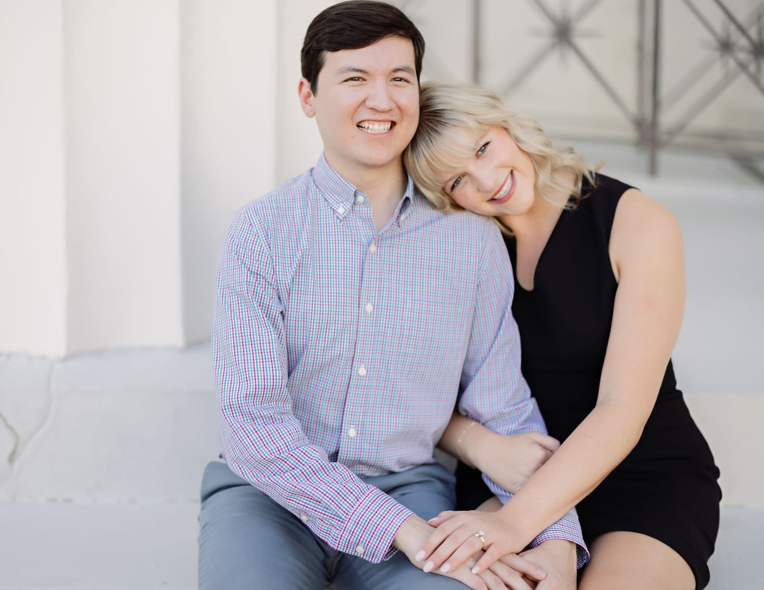 A couple in casual attire sharing a tender moment on a white architectural background.