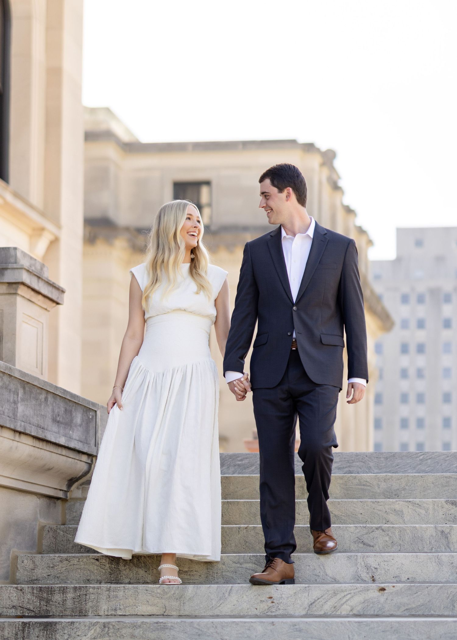 A couple in formal attire walking down stone steps together in an urban setting.