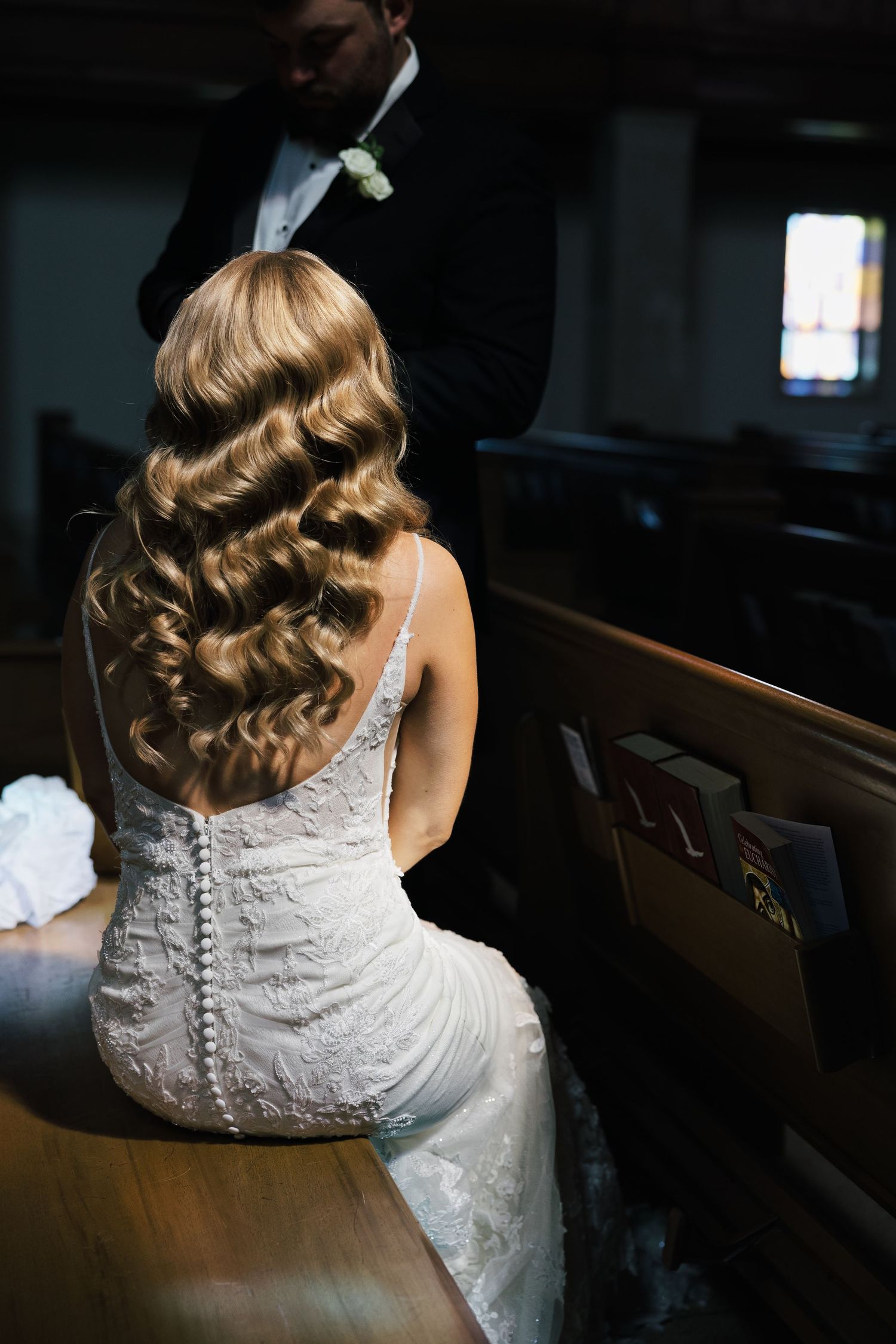 Detailed lace wedding dress and elegant curled hairstyle captured in church pews.