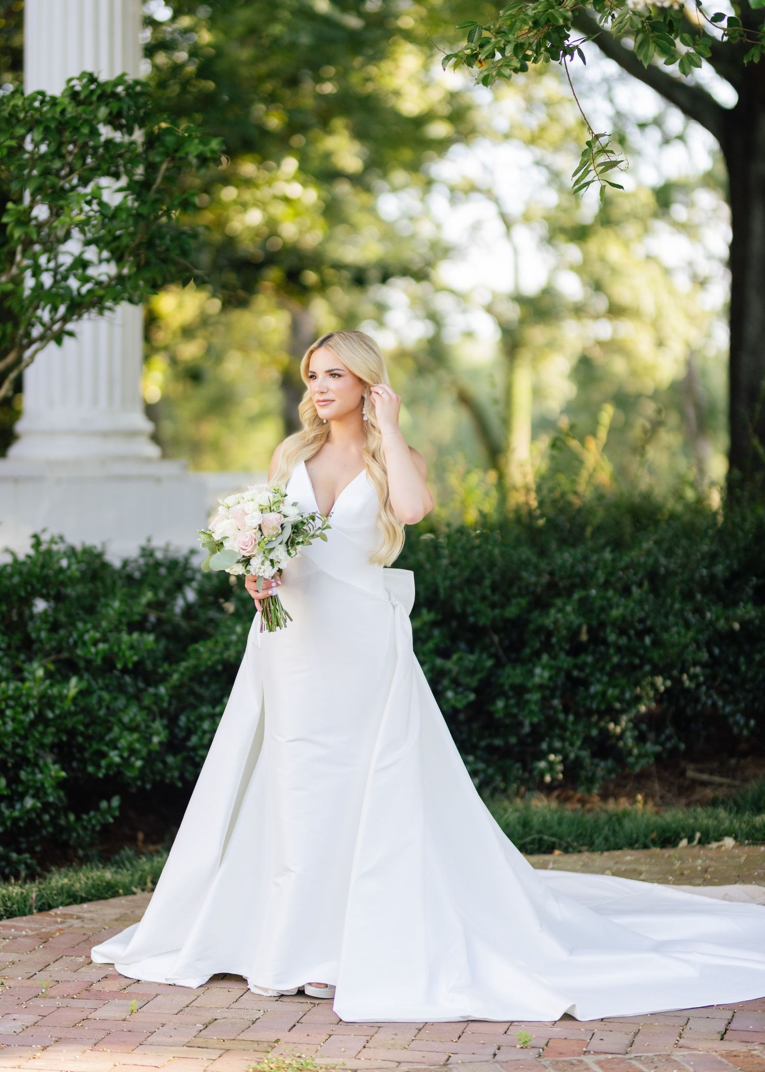 A white wedding gown flowing gracefully in a garden setting with classical columns.