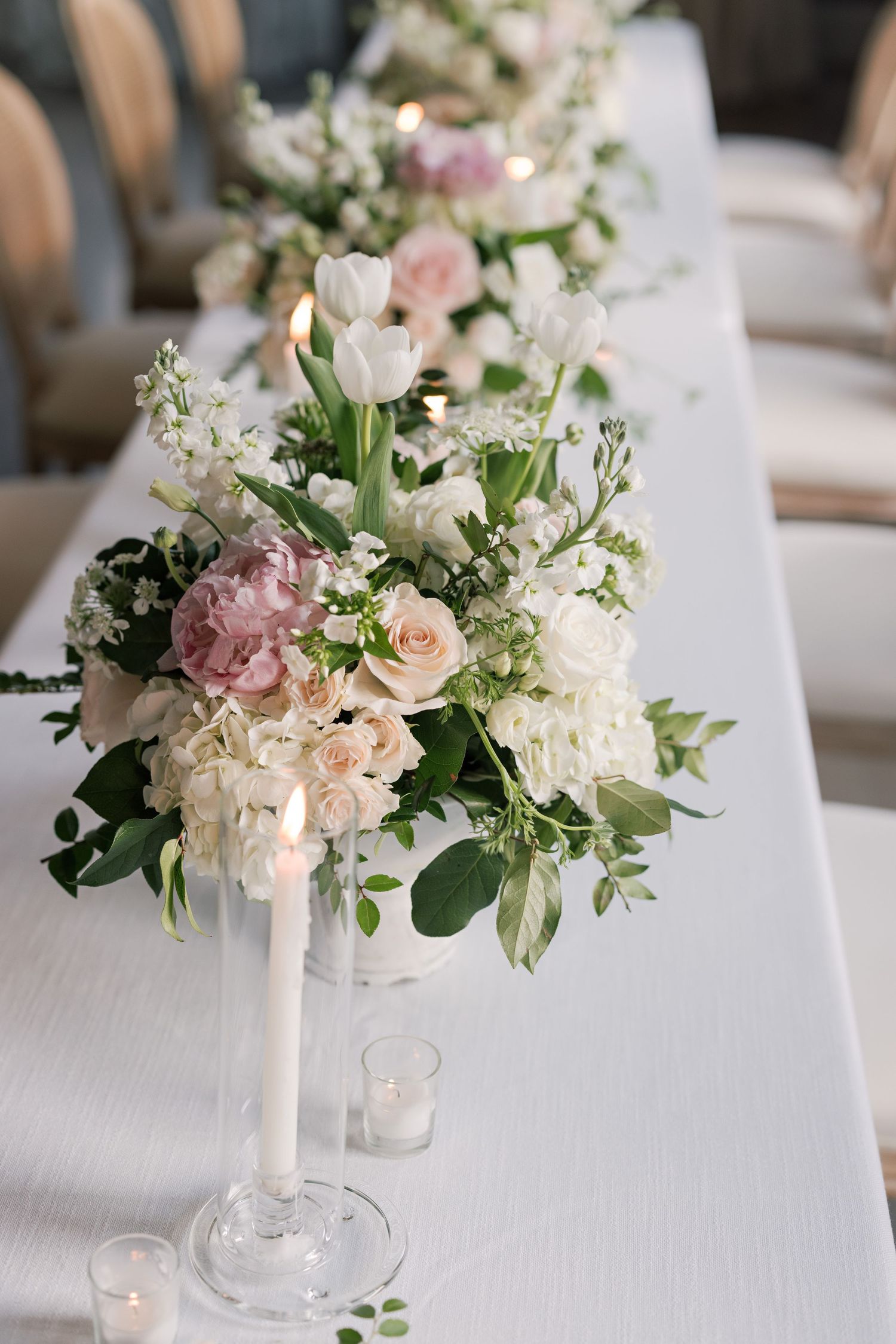 Close-up of romantic pastel floral arrangement with roses and tulips in a white candlestick holder.