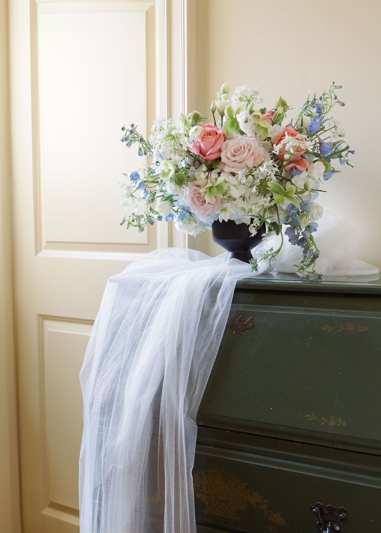 Delicate floral arrangement with roses and veil draped over dark piano.