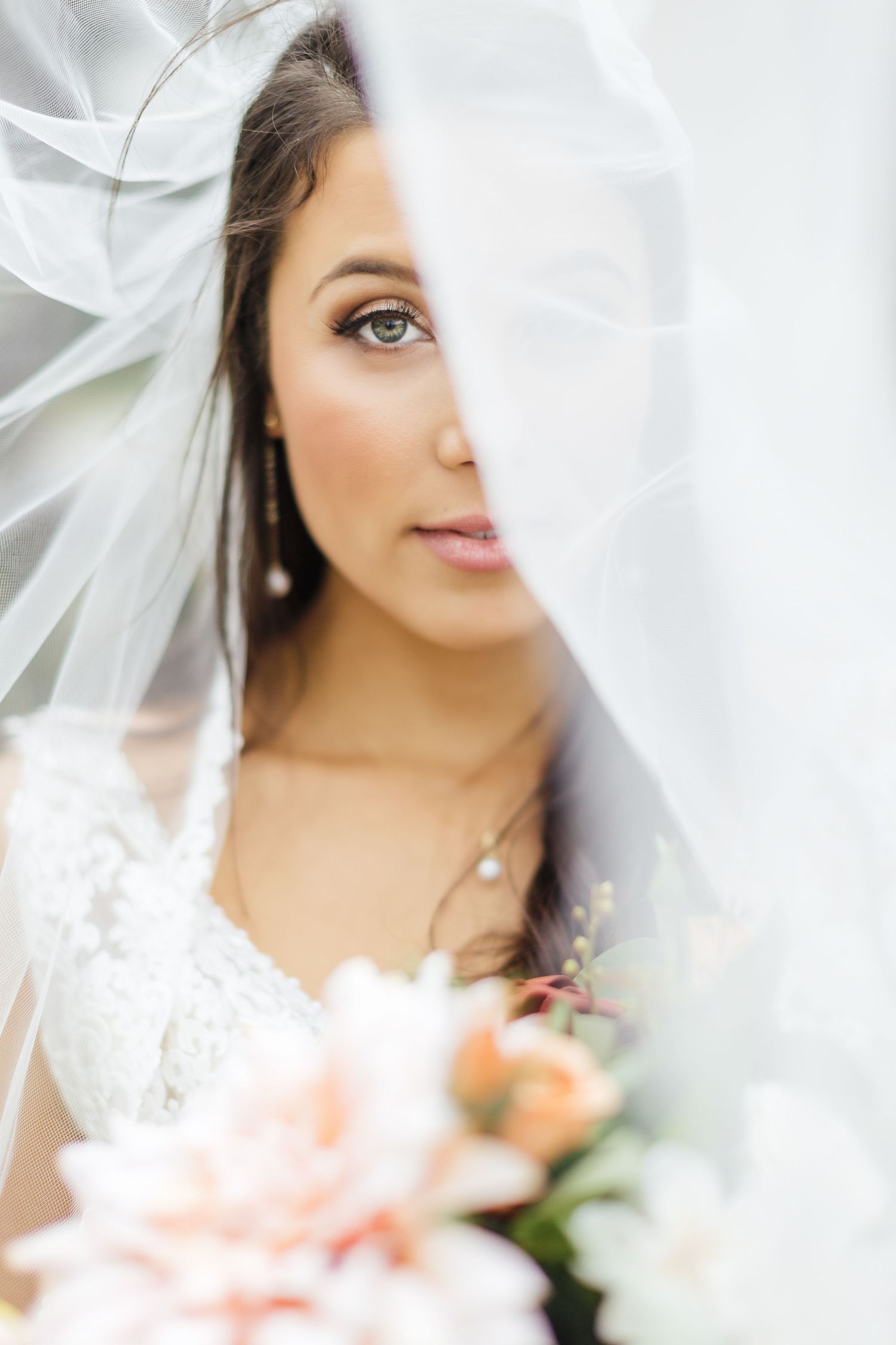 Soft focus artistic bridal portrait through delicate veil with peach florals.