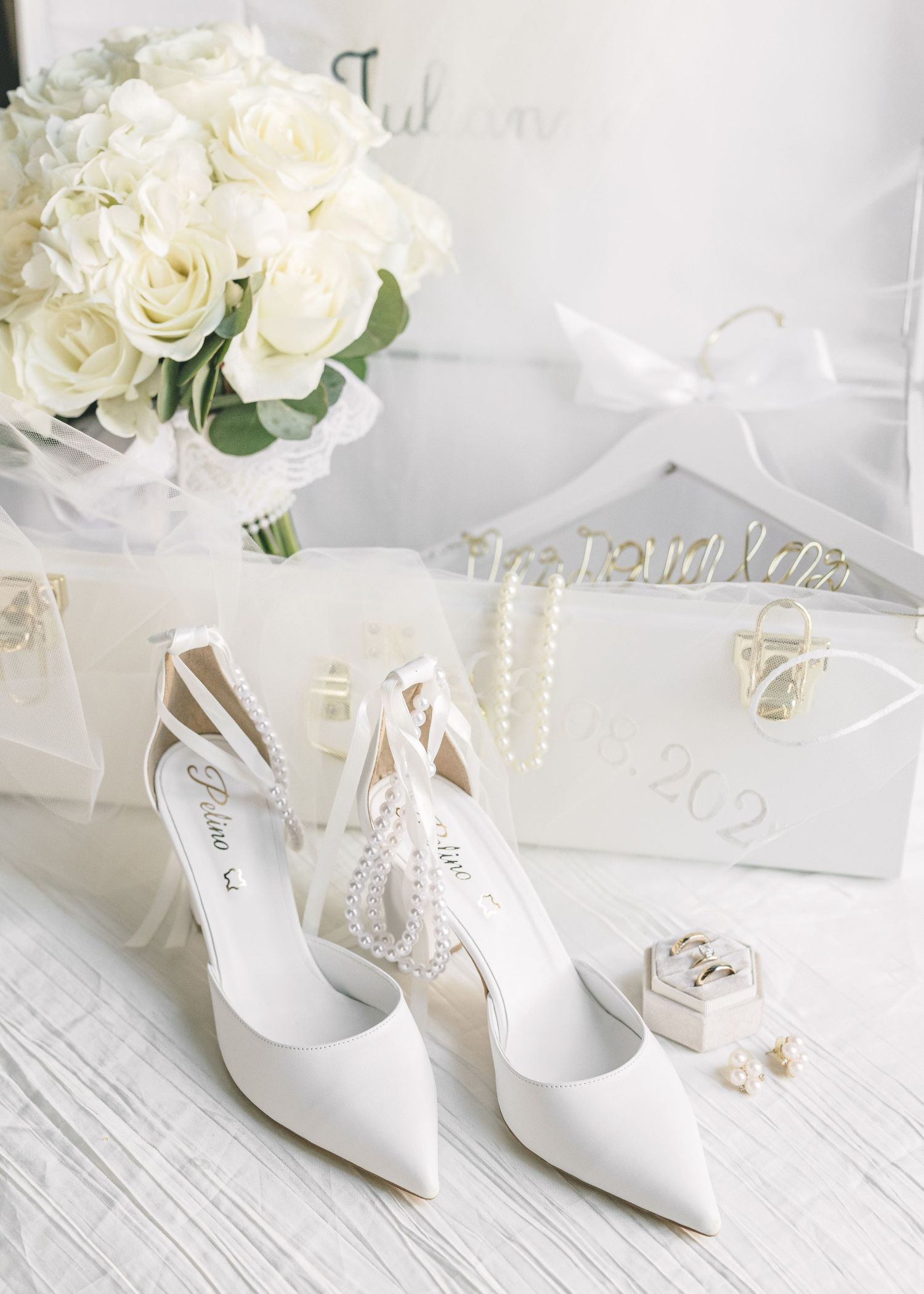 White bridal shoes and roses arranged on a rustic white wooden surface.
