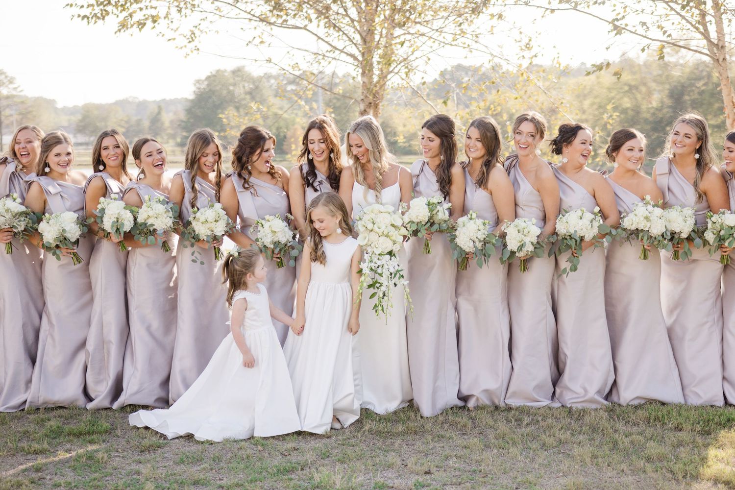 Row of bridesmaids in soft lavender dresses standing together outdoors against a natural backdrop.
