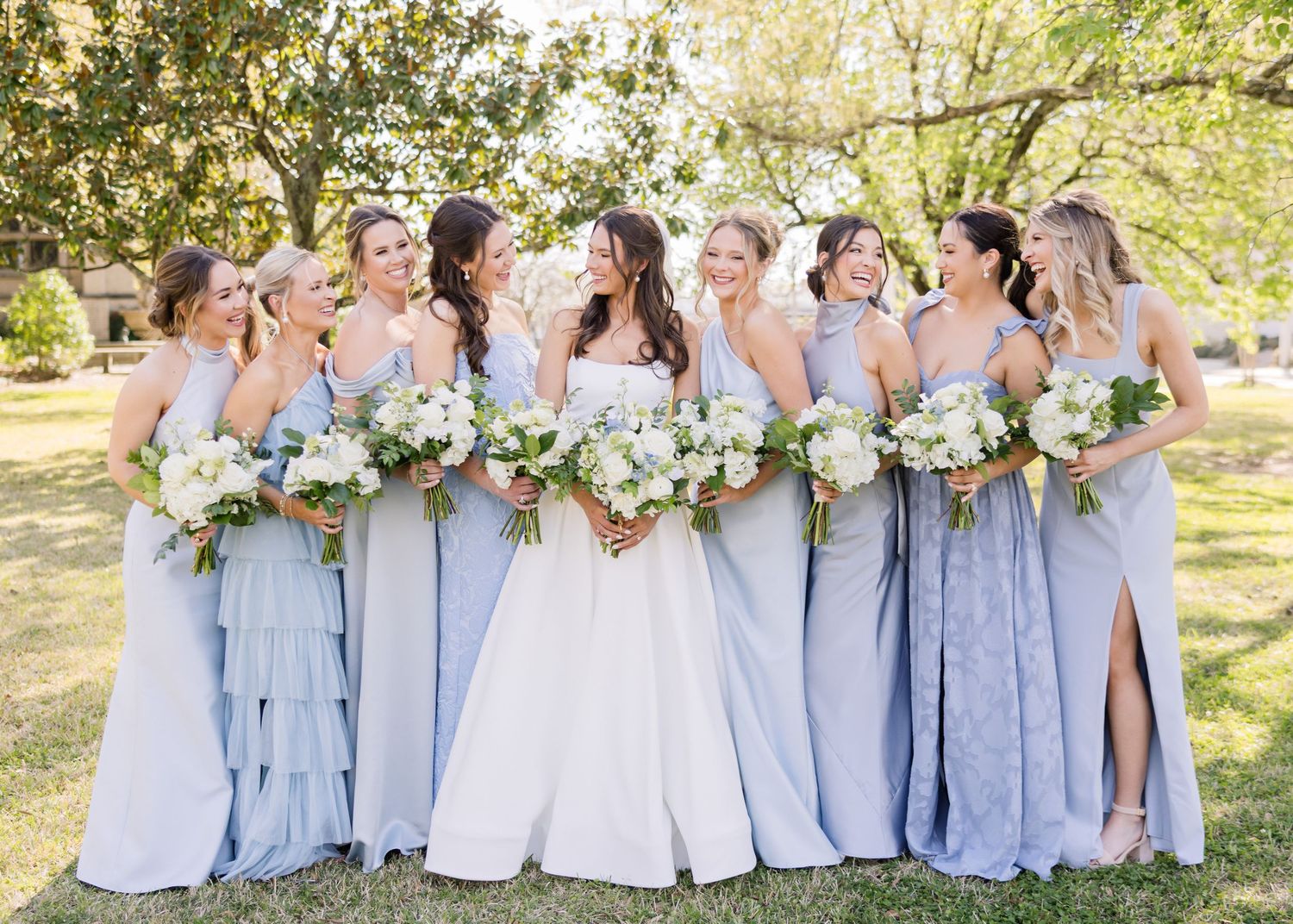 Wedding party in powder blue dresses lined up outdoors for formal group photo.