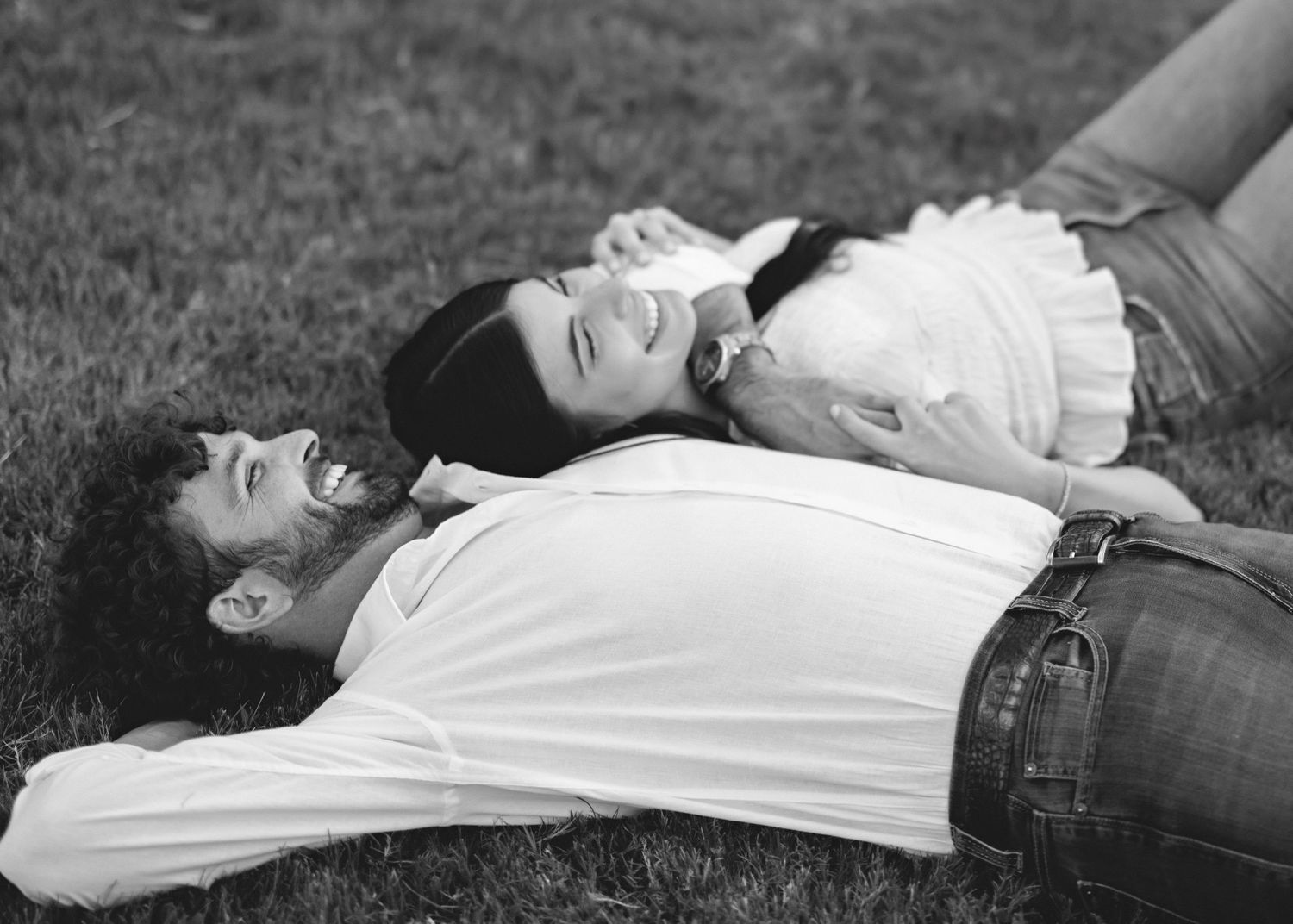 A couple laying on grass together sharing an intimate black and white moment.