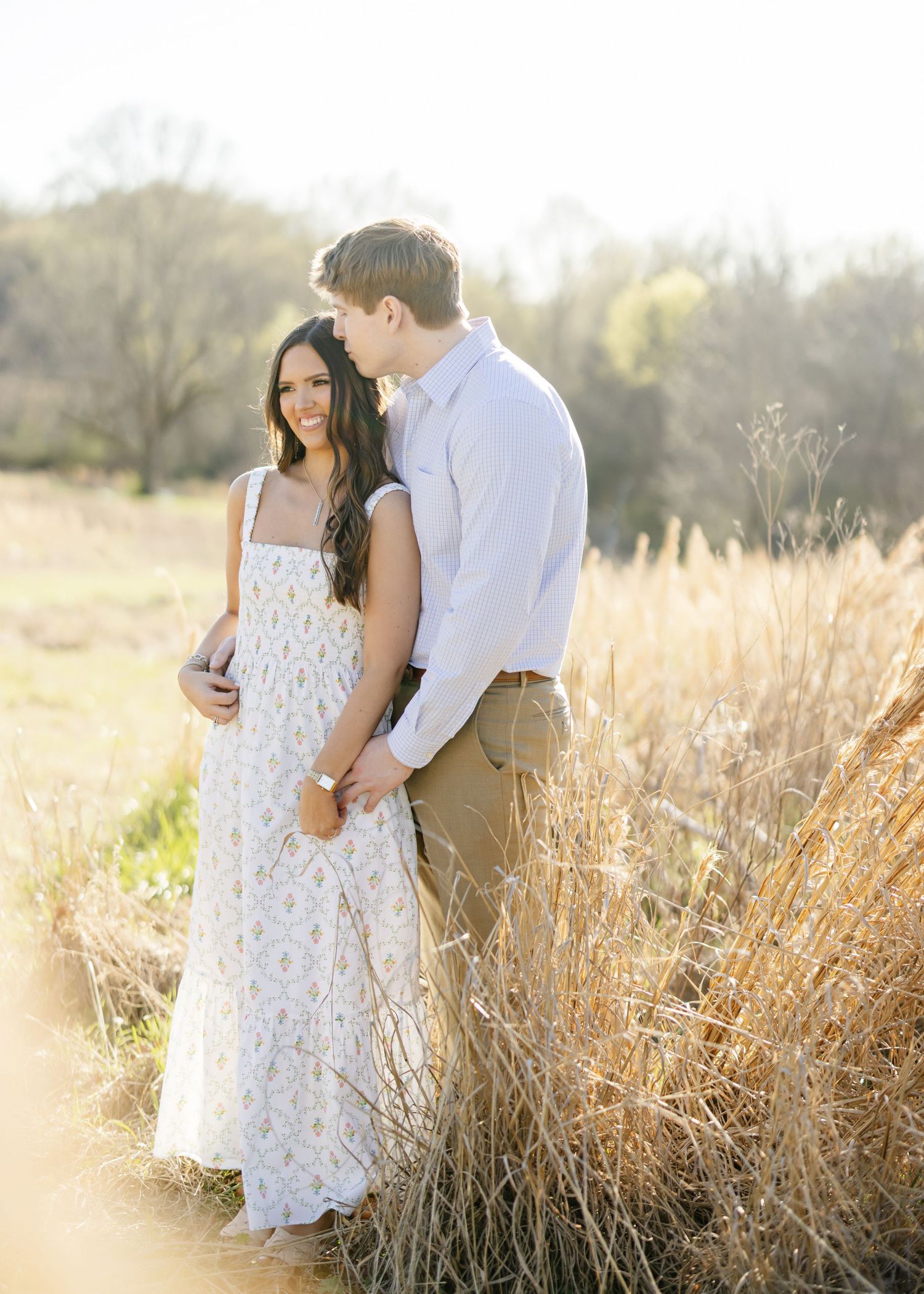 Intimate moment between couple in sunlit field with tall grass.