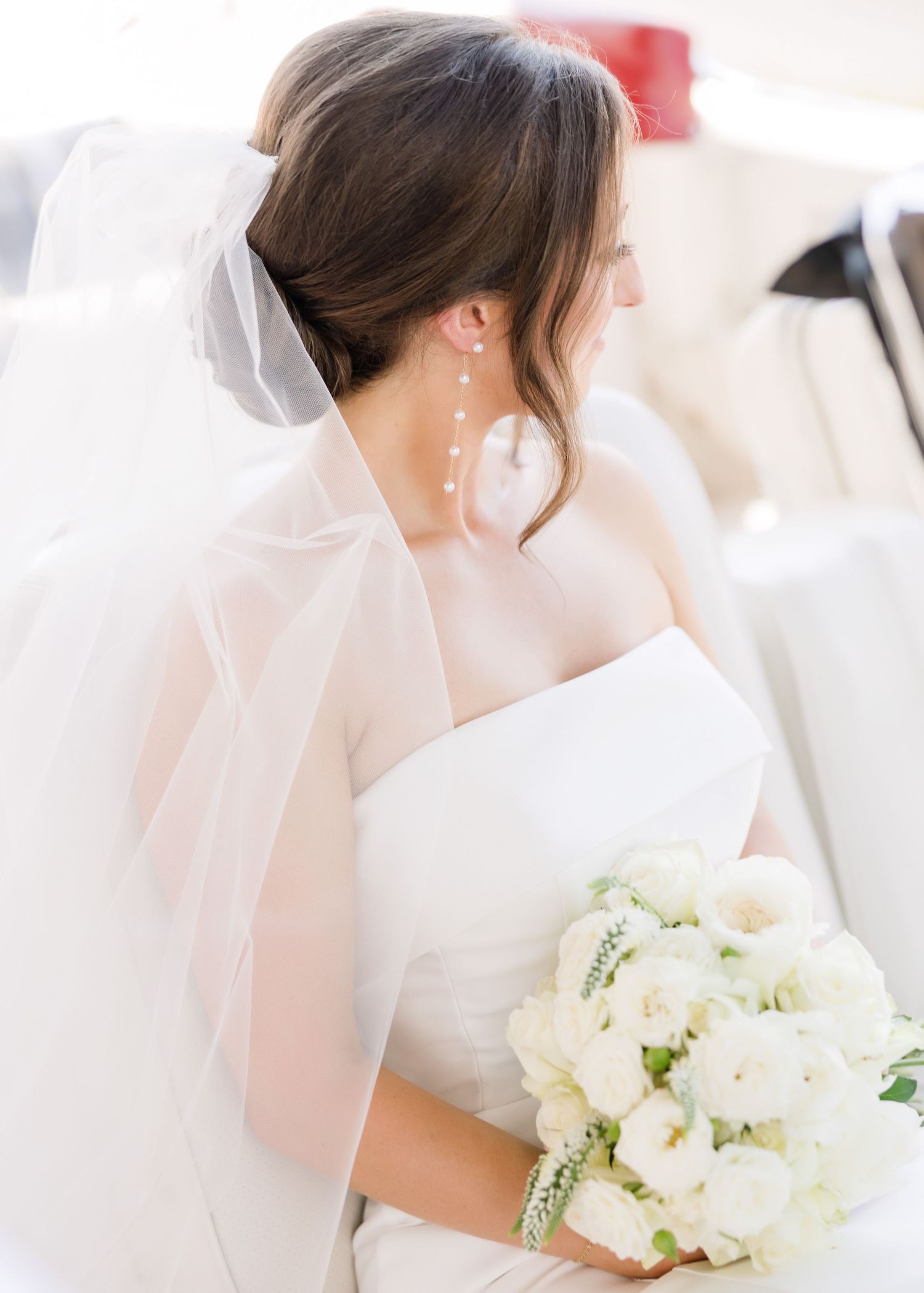 A bride in a white wedding dress holds an elegant bouquet of white flowers against a light background.