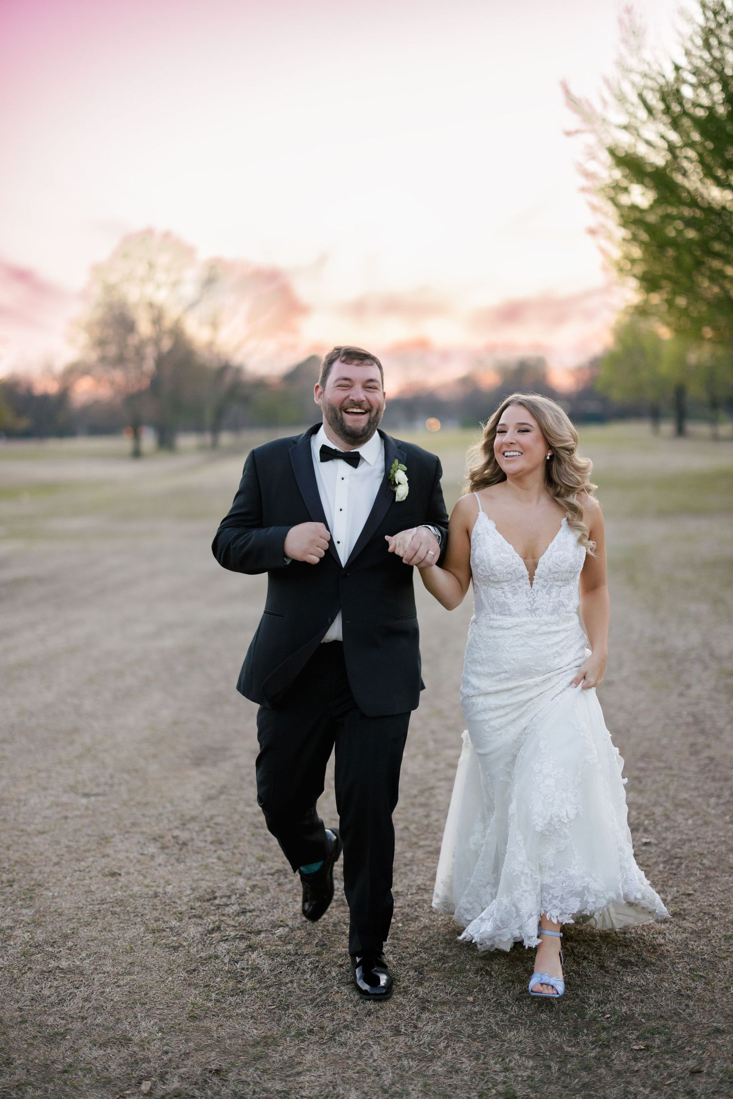 A couple runs joyfully across an open field at sunset during their wedding celebration.