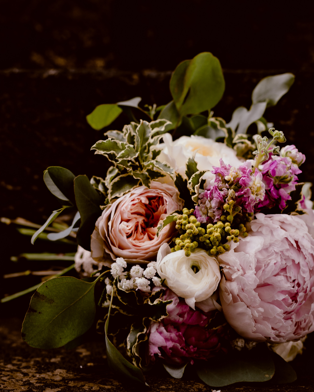 Romantic bouquet with pink peonies, roses and greenery on dark background.