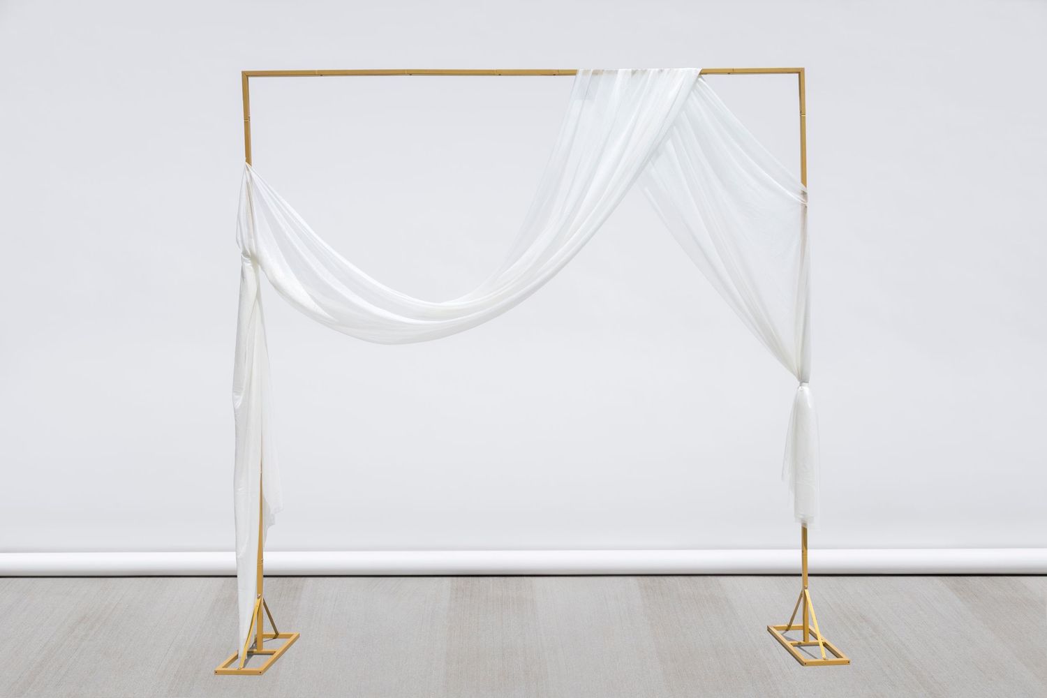 White fabric drapes elegantly across a gold metal frame against a minimalist white backdrop.