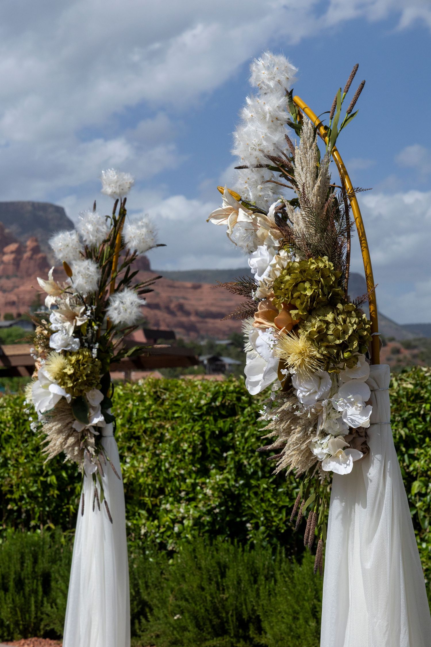 Two floral wedding arch pillars with white blooms and pampas grass against red rock landscape in Sedona, Arizona.