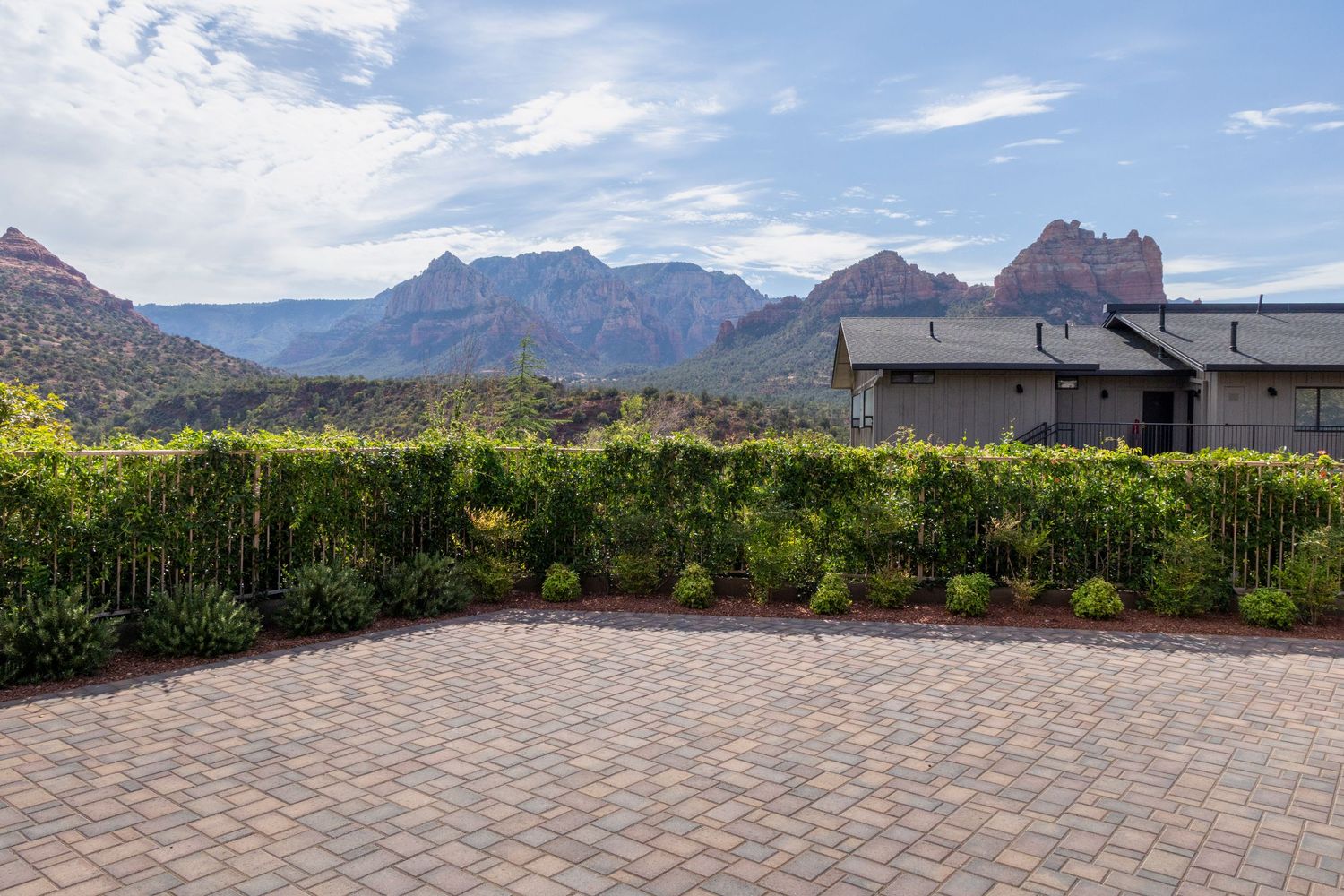 Paver patio with lush green hedges and stunning red rock mountain views under a partly cloudy sky in Sedona, AZ.