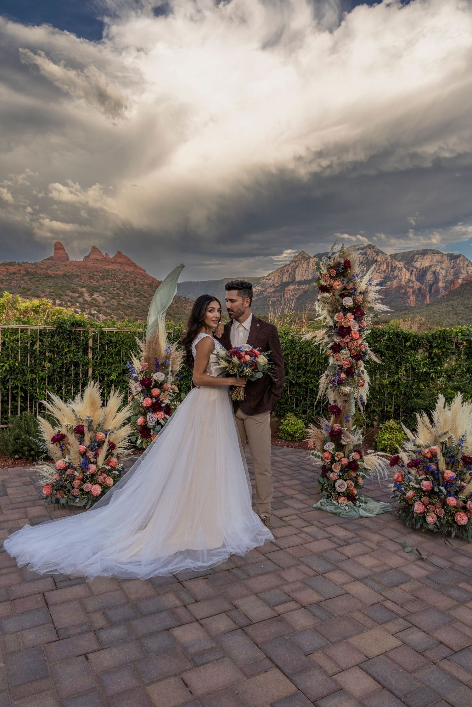 A romantic outdoor wedding ceremony in Sedona with dramatic red rock formations and cloudy skies in the background.
