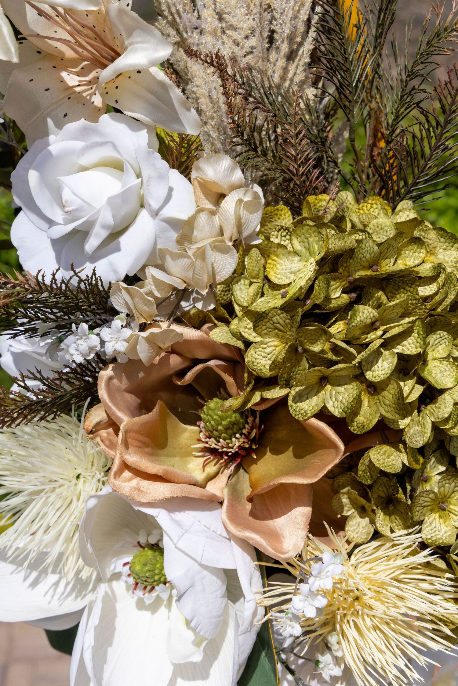 Elegant floral arrangement featuring white roses, green hydrangeas, peach magnolias, and dried grasses in a natural earthy bouquet.