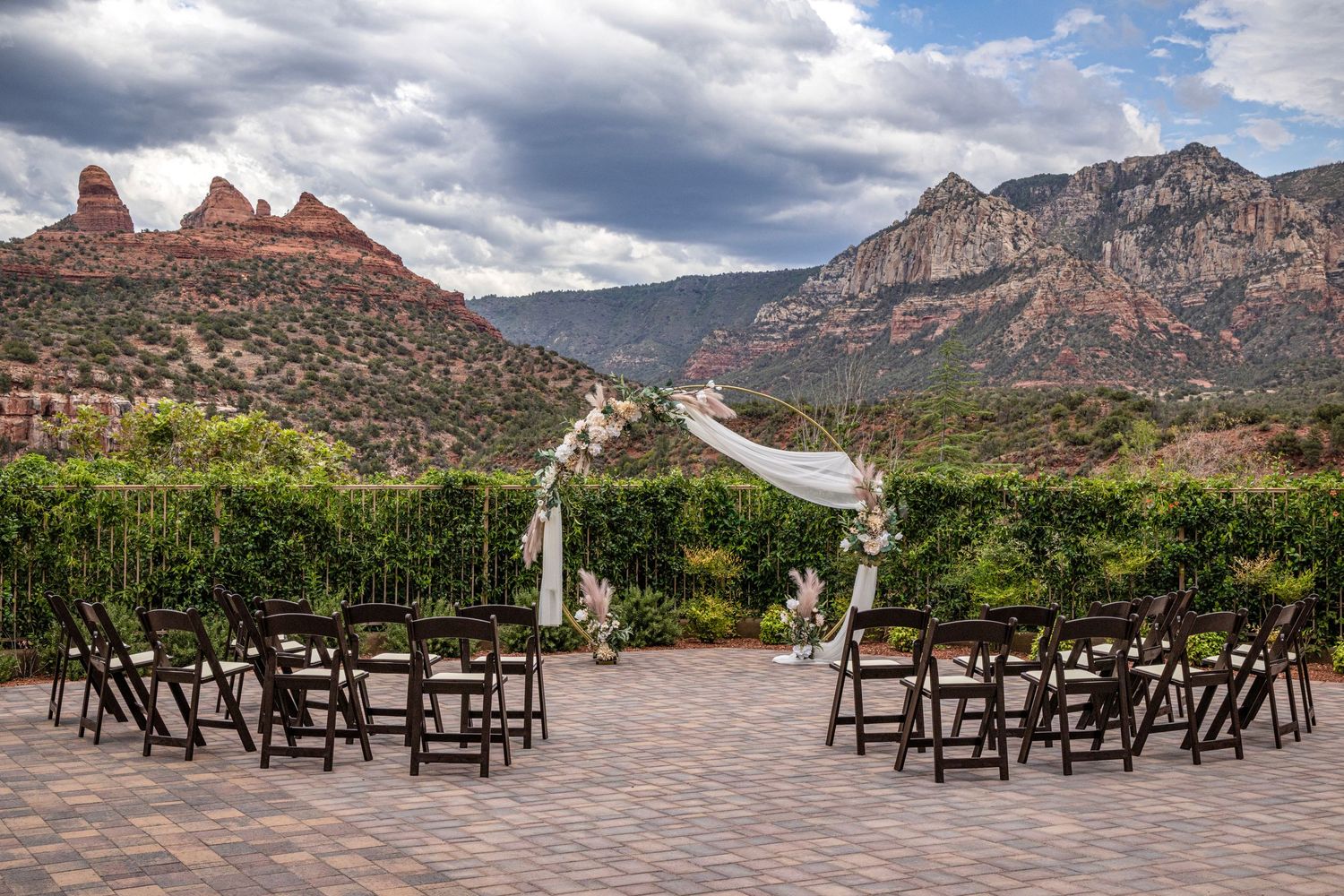 A row of wooden lounge chairs facing scenic red rock mountains in Sedona under dramatic cloudy skies.