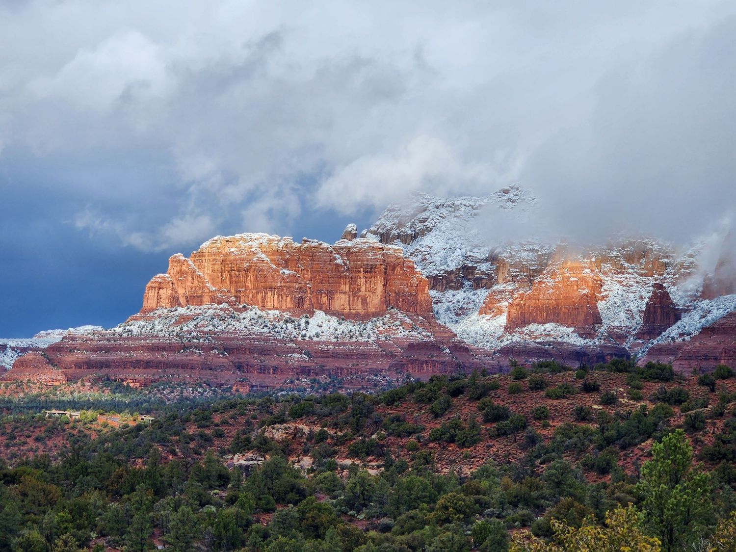 Snow-dusted red rock formations rise dramatically against stormy clouds in Sedona, Arizona.