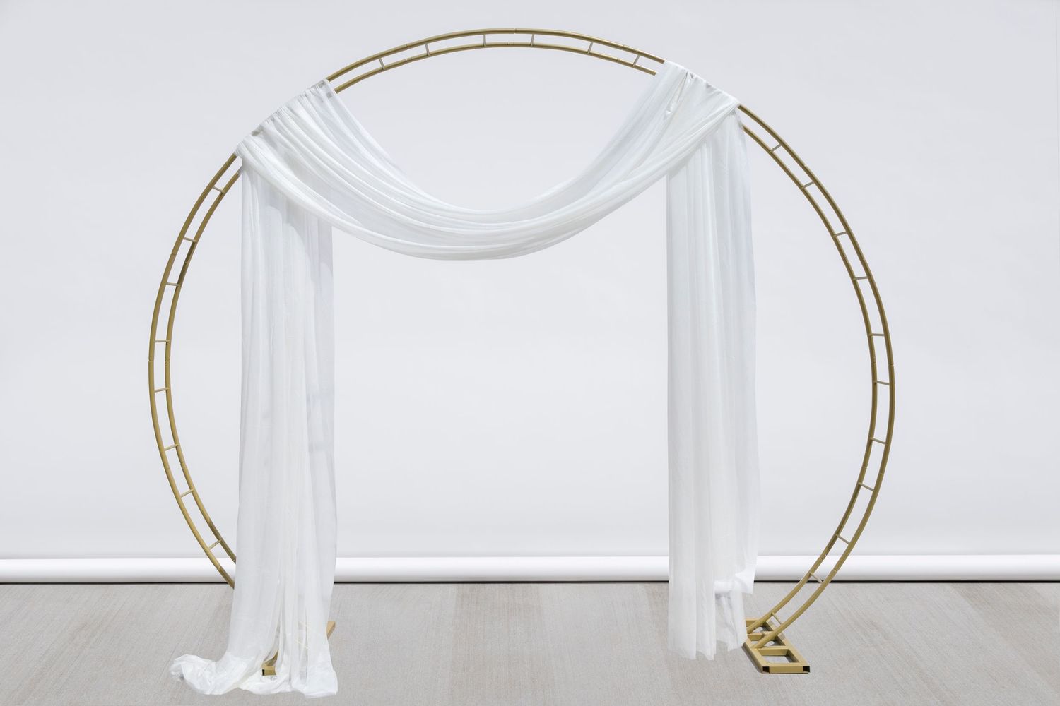 Circular gold arch with flowing white fabric drapes creates an elegant ceremony backdrop.