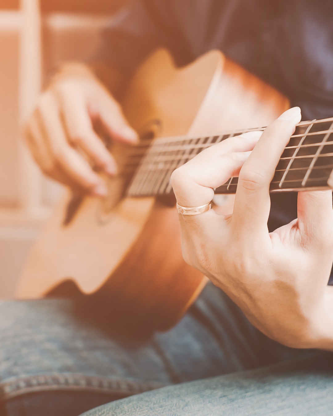 Close-up shot of hands playing acoustic guitar strings in warm lighting.