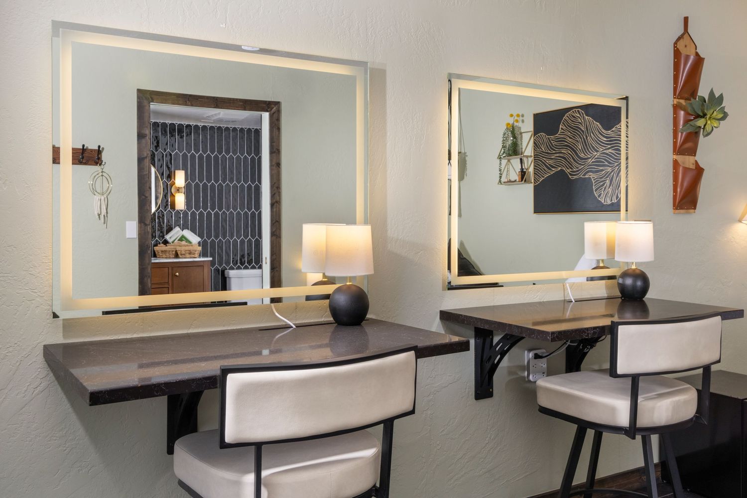 Two elegant vanity desks with illuminated mirrors, white chairs, and decorative lamps in a modern hotel room.
