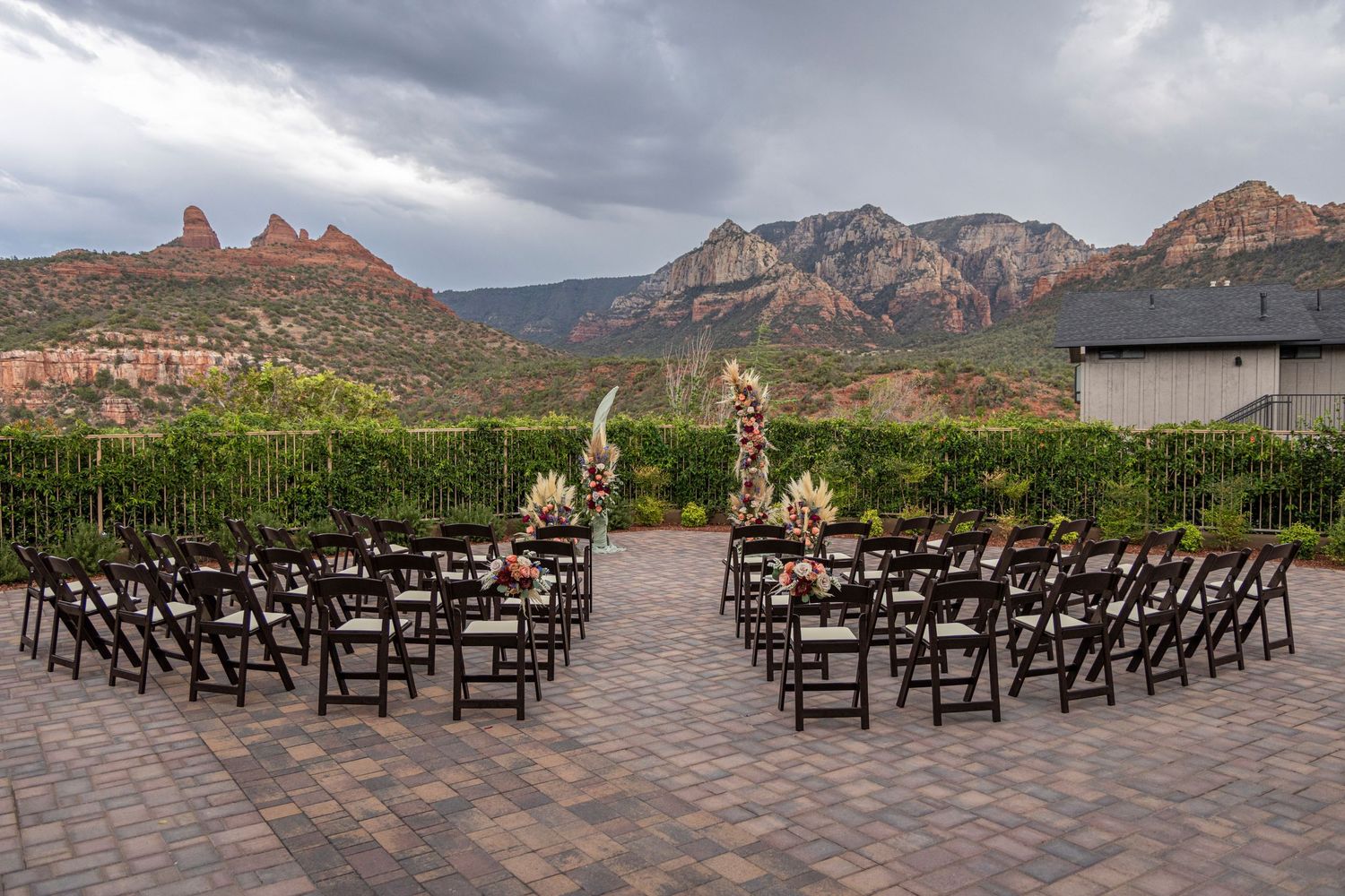 Outdoor wedding ceremony setup with rows of dark wooden chairs facing red rock mountains in Sedona under dramatic clouds.