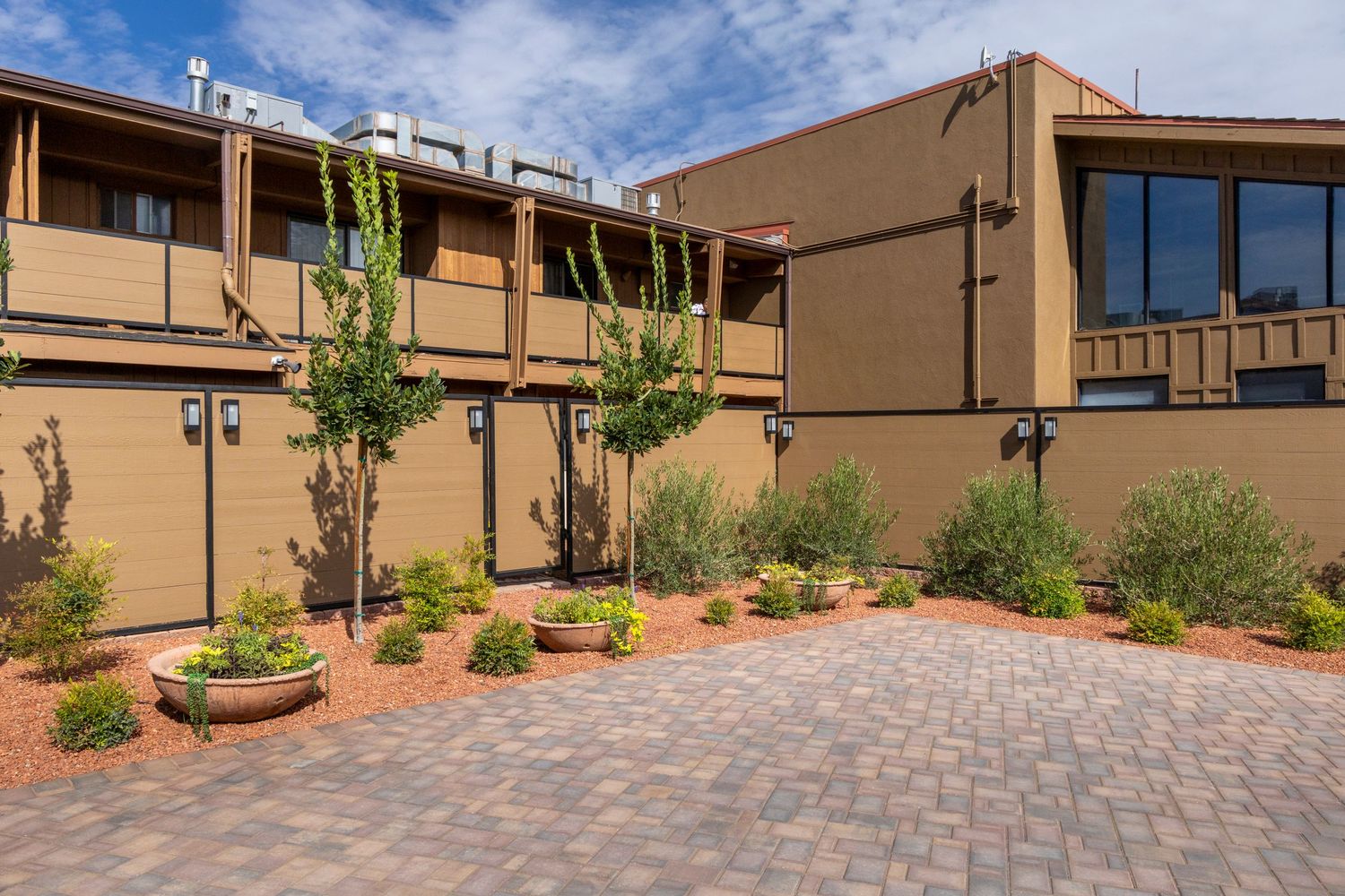 Curved paver walkway with desert landscaping leads to modern tan stucco buildings under bright blue sky.