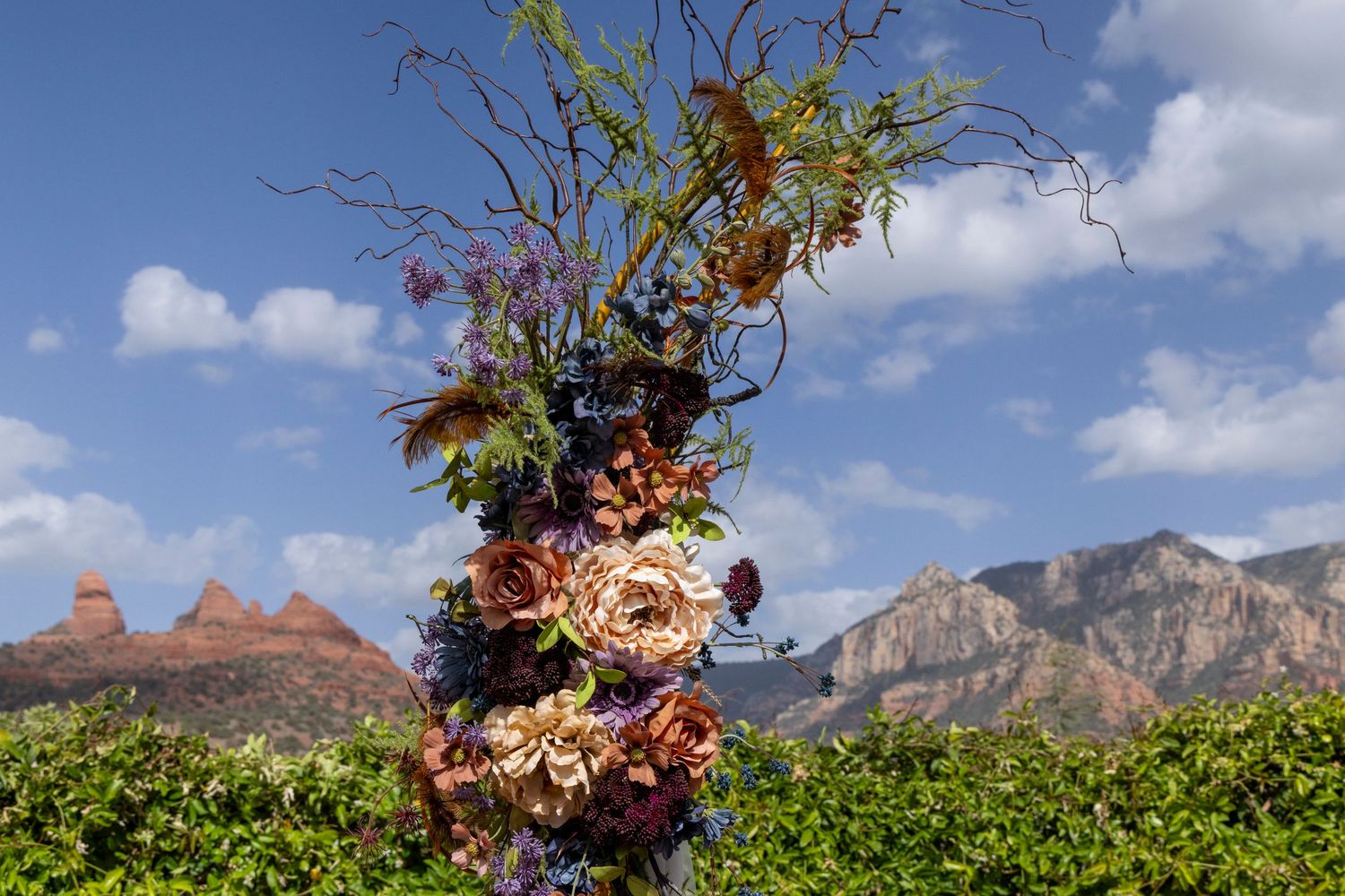 Elaborate floral arch with colorful blooms and twisted branches against Sedona red rock mountain backdrop.