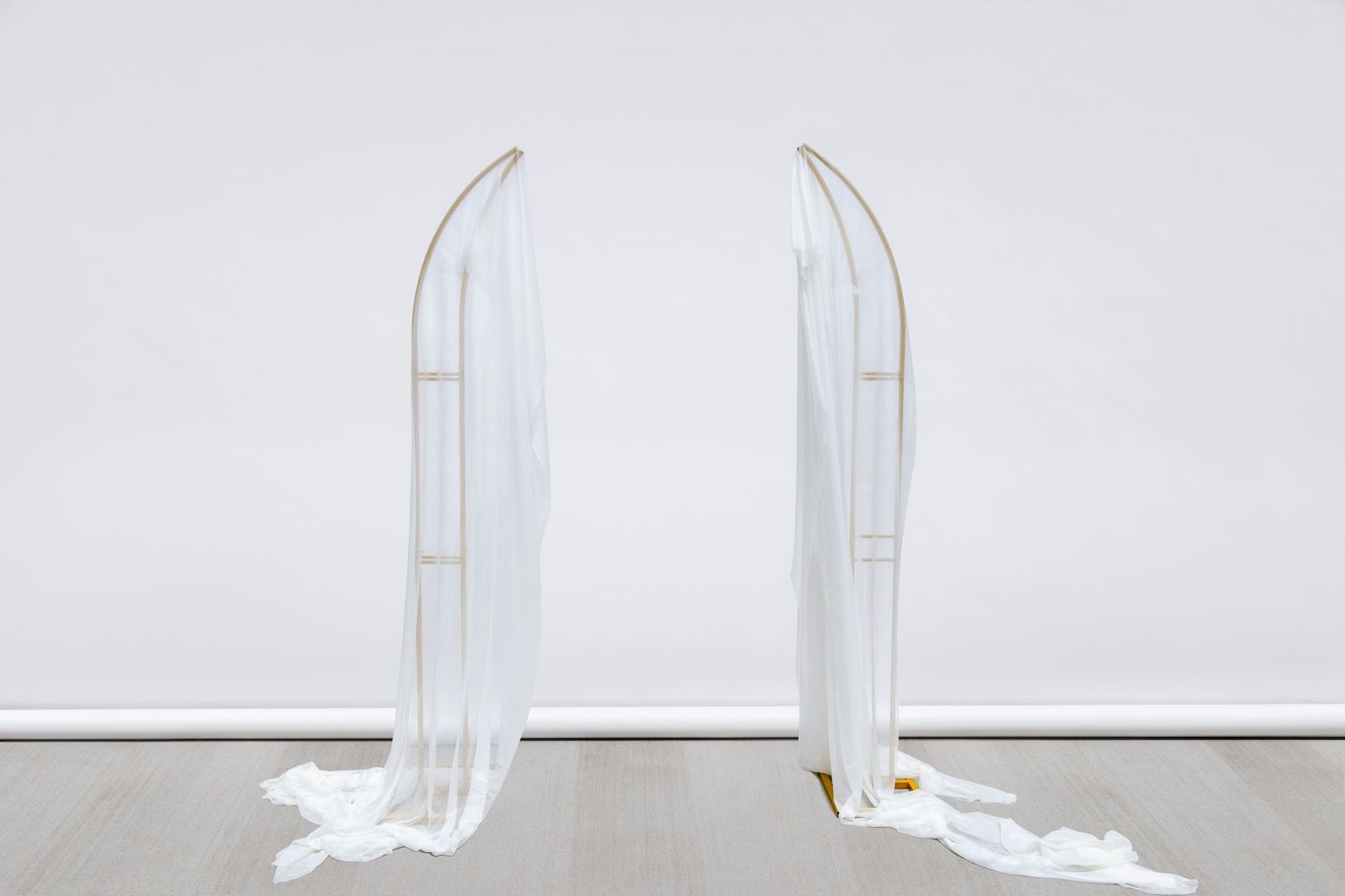 Minimalist gold frame arch with flowing white fabric panels creates vertical design.