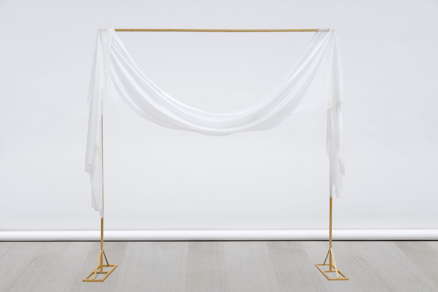 Simple gold frame with single swooping white fabric drape creates elegant wedding arch display.