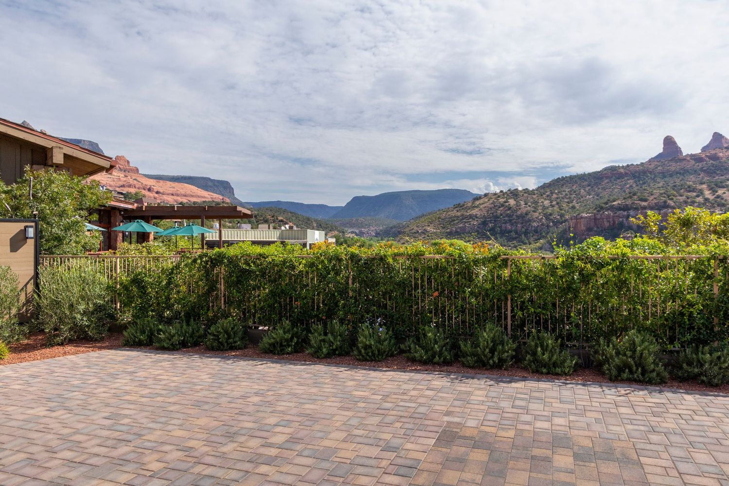 Brick paved patio with lush green hedges and stunning red rock mountain views under a partly cloudy sky in Sedona, AZ.