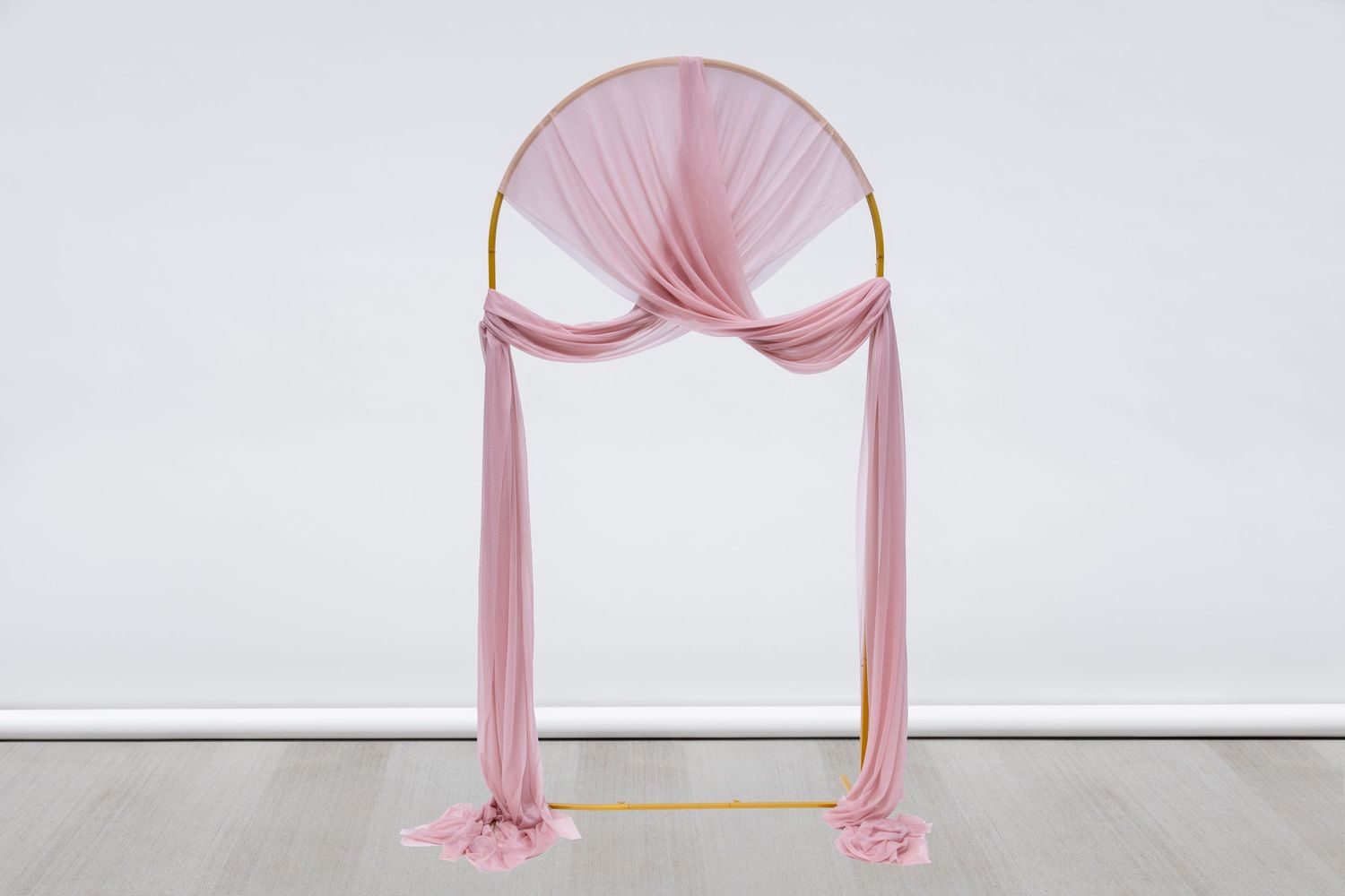 Delicate pink fabric arch display with graceful draping against white background.