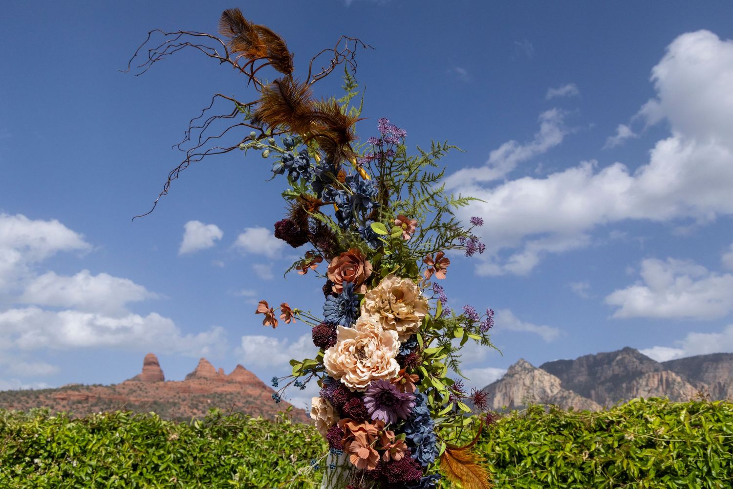 Stunning tall floral arrangement with roses and wildflowers against a dramatic red rock desert landscape backdrop.