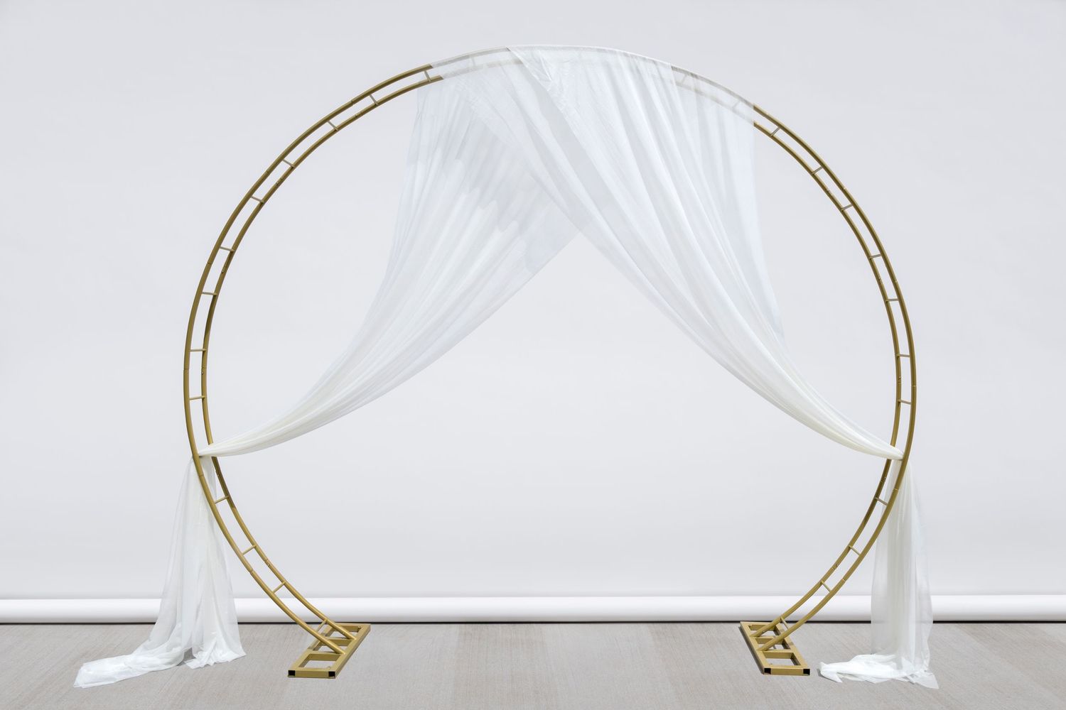 Circular gold ceremony arch with draped white fabric and geometric base stands elegantly.