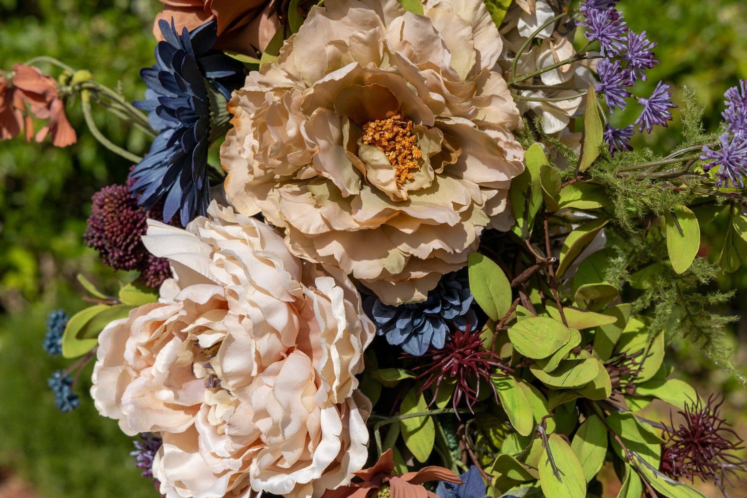 Close-up of a lush floral arrangement featuring cream peonies, navy blue flowers, and deep burgundy blooms with green foliage.