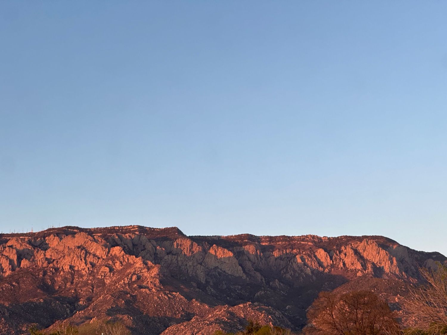 Scenic mountain range glowing orange and red at sunset with rugged peaks against a blue sky.
