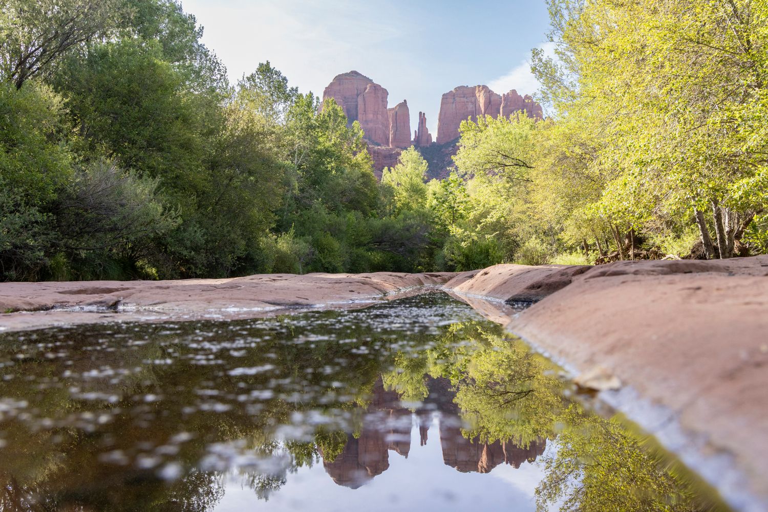 Scenic red rock formations and lush trees reflect in the calm waters of Oak Creek at Sedona, Arizona during sunset.
