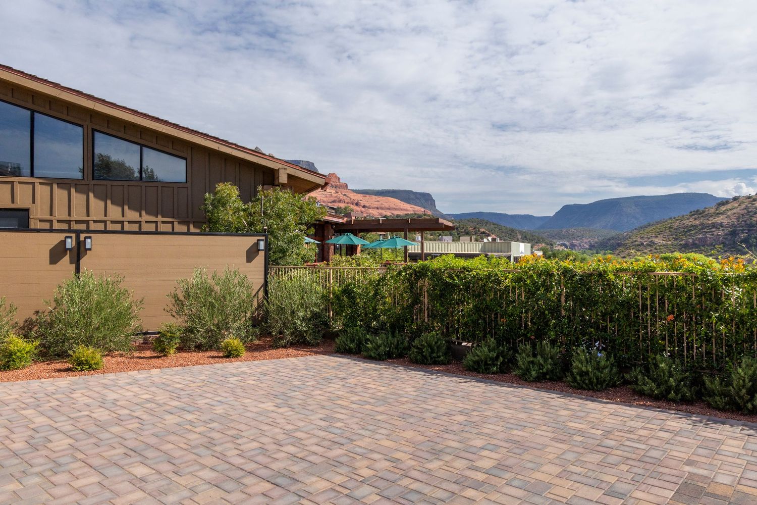 Panoramic view of a modern hillside property with paver stone driveway and desert mountain landscape in the background.