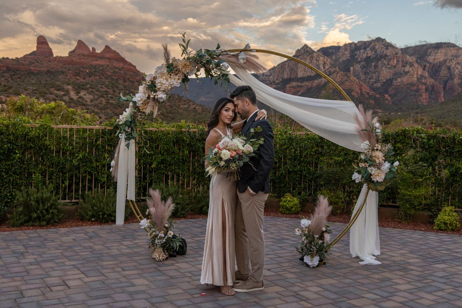 A scenic outdoor wedding ceremony setup with white fabric draping and floral arrangements against dramatic red rock mountains.