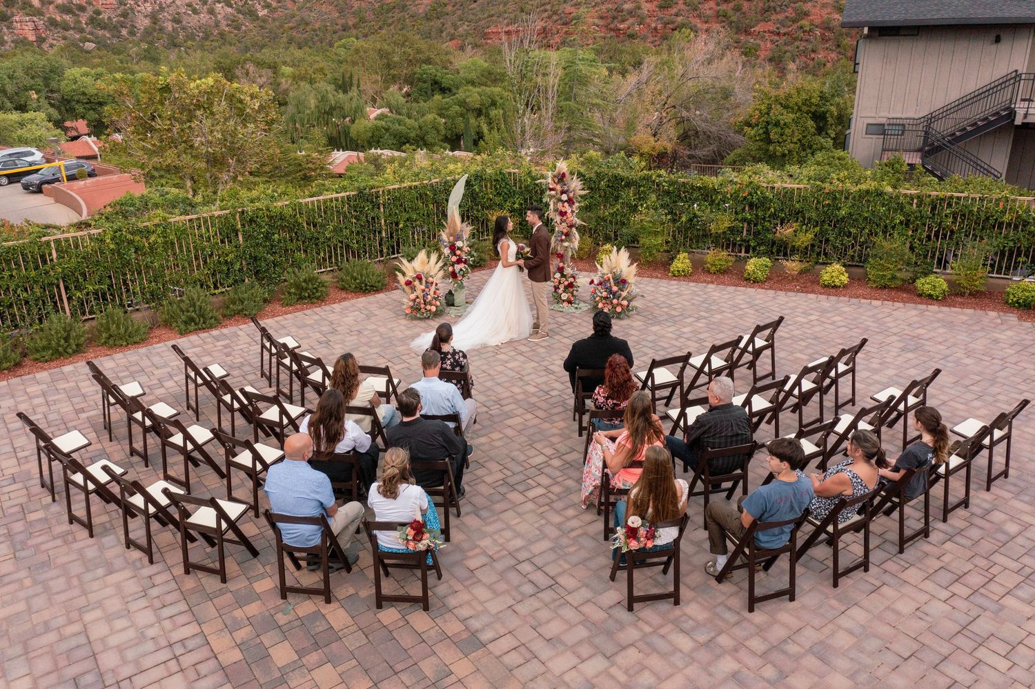 Outdoor wedding ceremony setup with wooden chairs arranged in rows on a brick patio surrounded by autumn foliage.